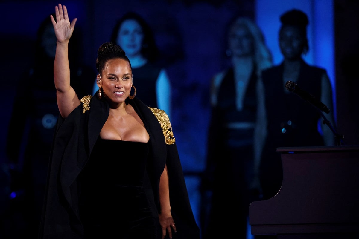 Alicia Keys raising her arm smiling while wearing a black dress.