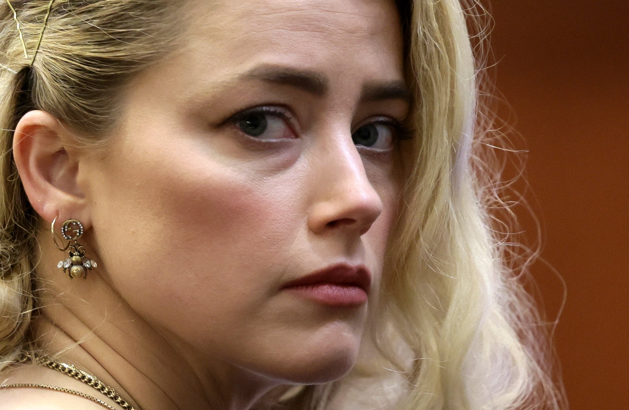 Amber Heard awaiting to hear the juror verdict in the Johnny Depp defamation case. A close-up on her face, looking to the side.