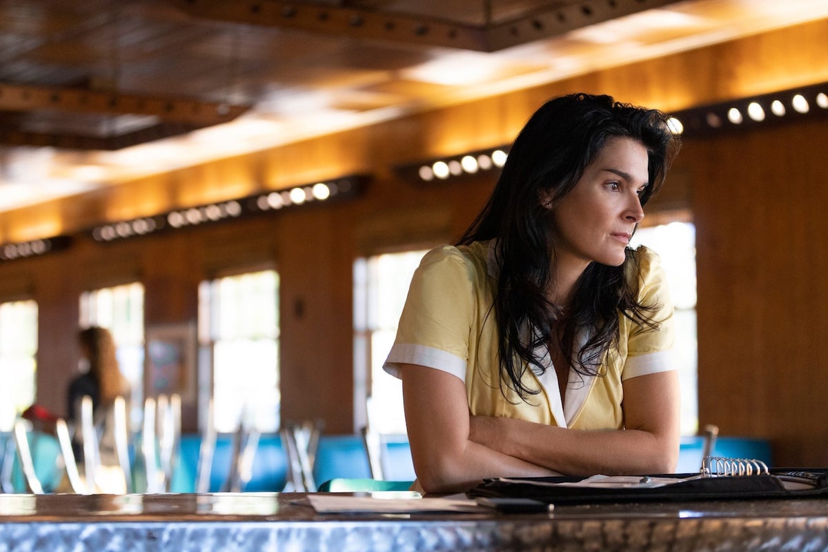 Angie Harmon, dressed as a waitress and leaning on a counter, in 