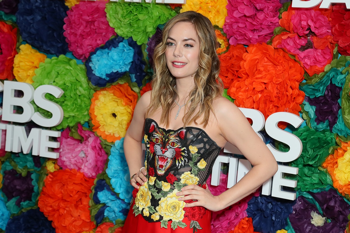 'The Bold and the Beautiful' star Annika Noelle wearing a red dress and posing in front of a floral hedge.