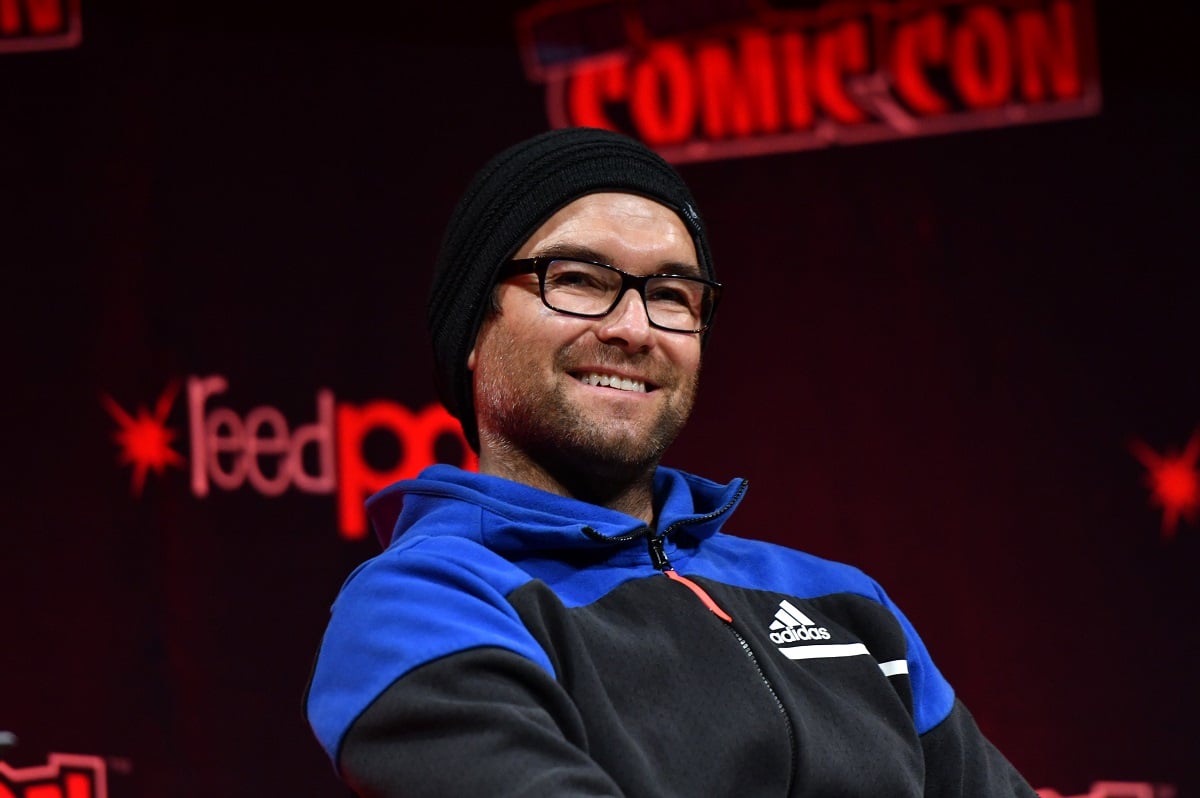 Antony Starr smiling while wearing a hat and a pair of glasses.