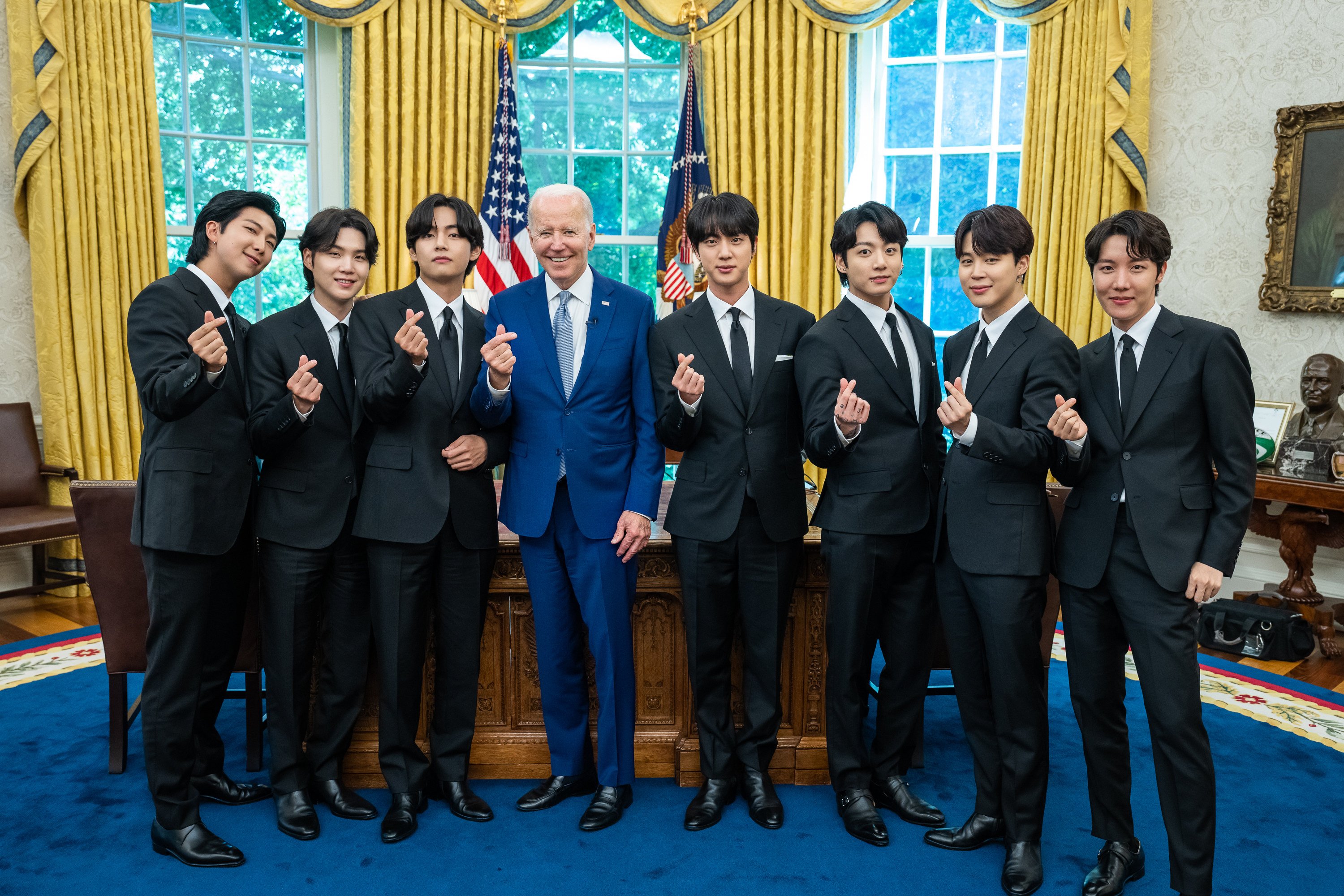 The members of BTS and President Joe Biden hold up finger hearts in the Oval Office