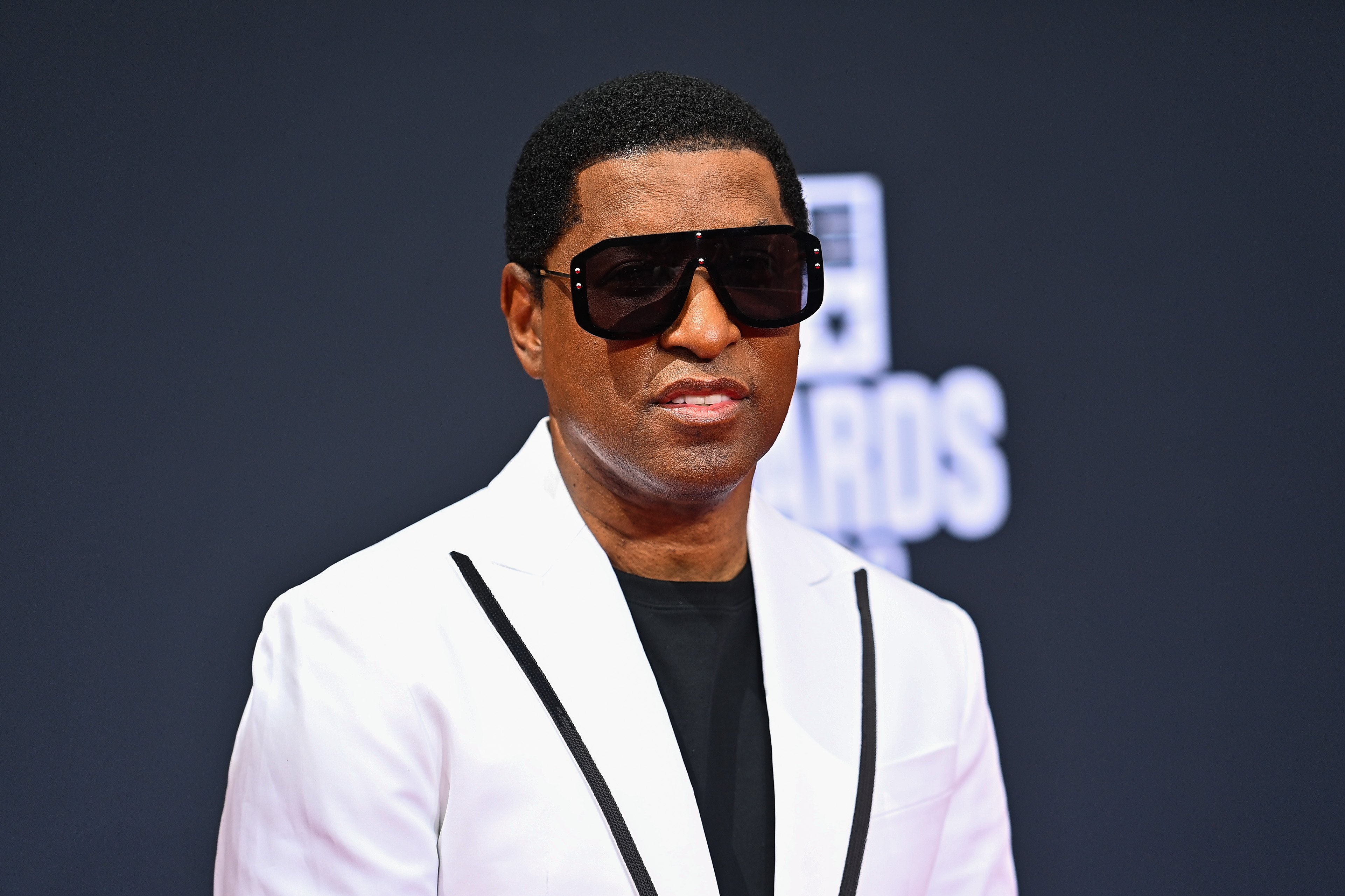 Singer and producer Kenneth Edmonds, known by his nickname Babyface, wearing a white suit and black sunglasses.