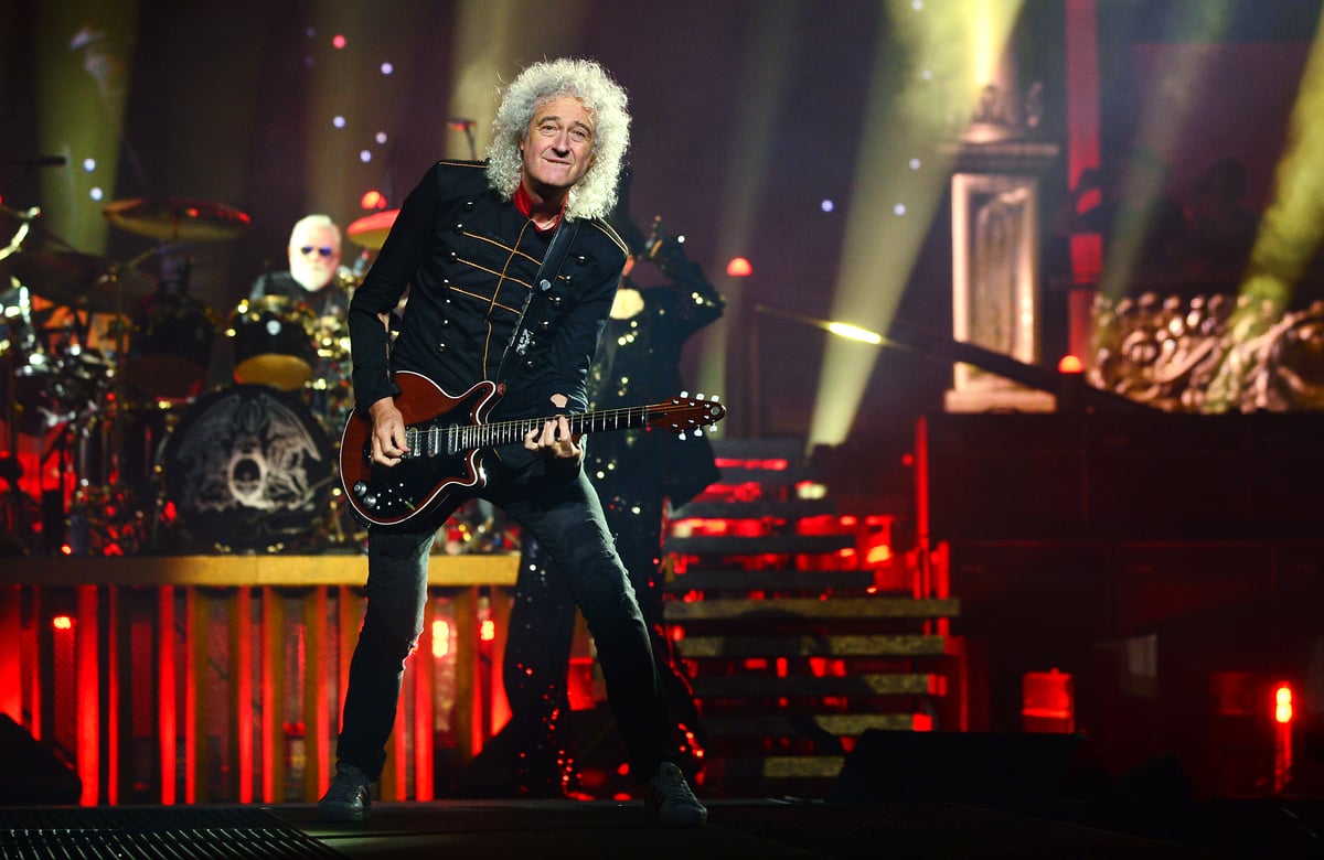 Brian May plays guitar on stage as a member of Queen.