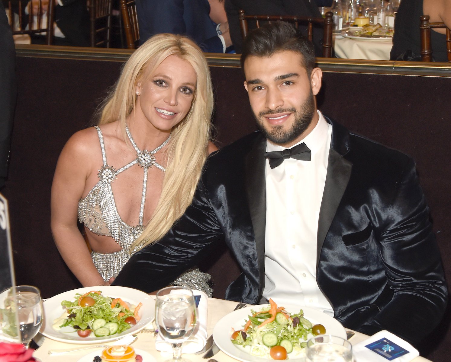 Britney Spears and Sam Asghari sitting at a table and smiling at an event