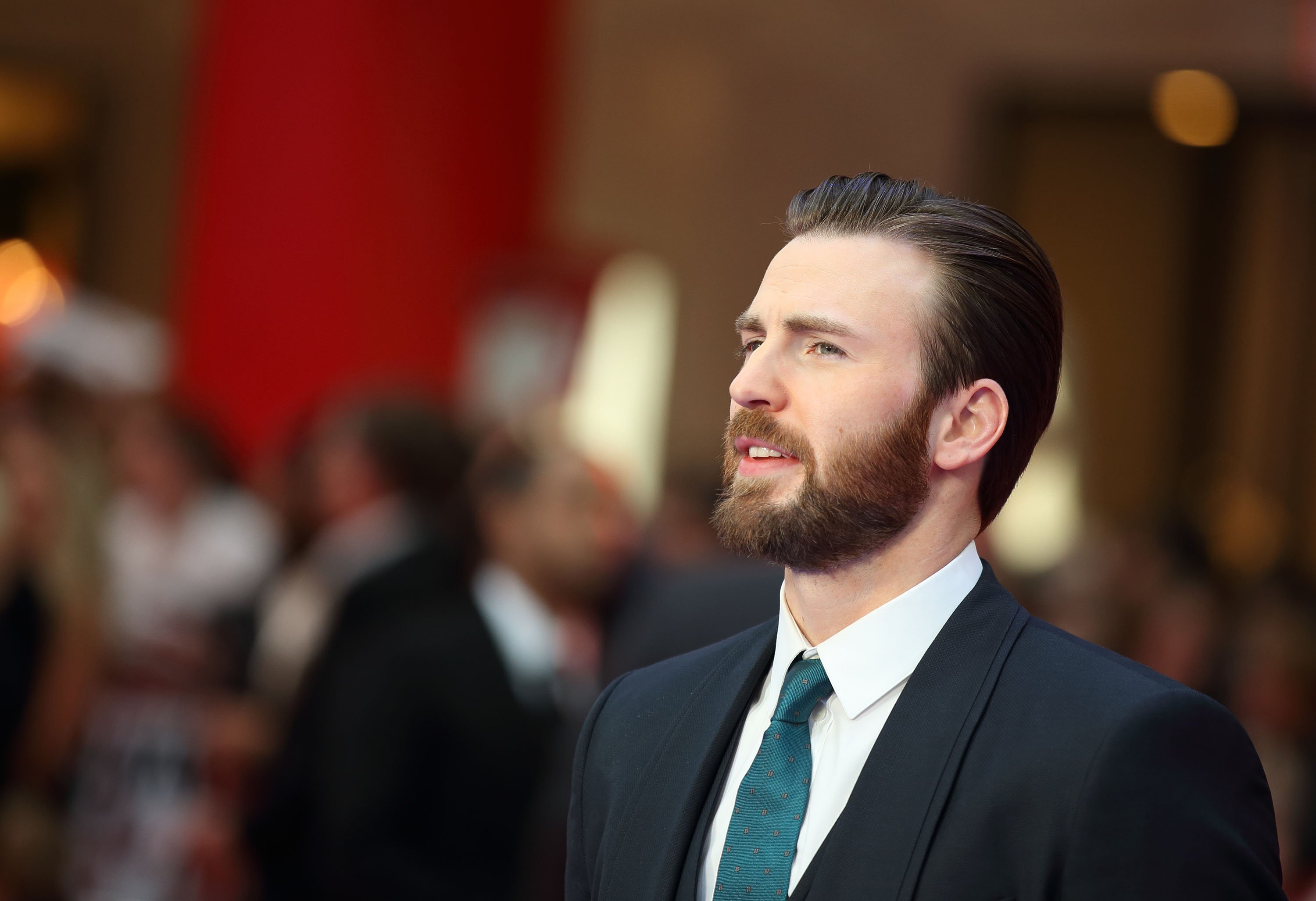 Captain America actor Chris Evans wearing a suit and posing at a film premiere.