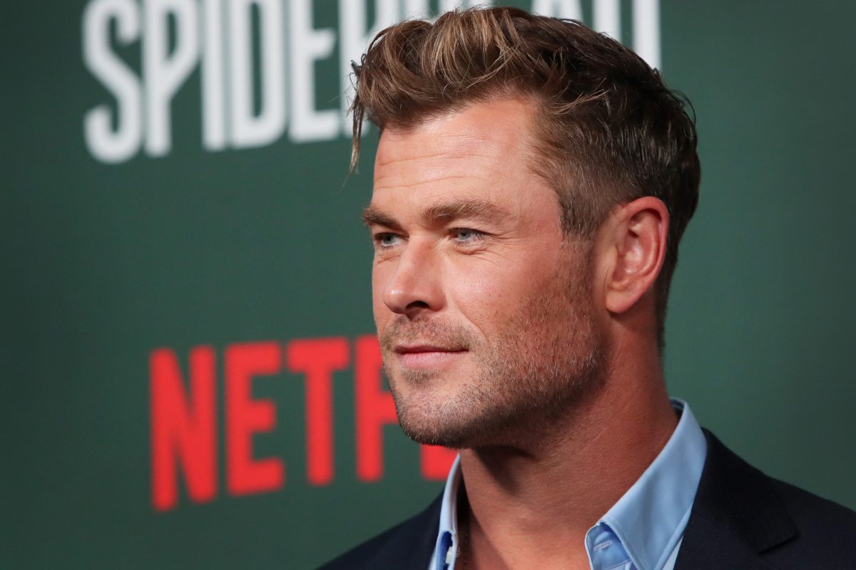 Chris Hemsworth, who stars as Thor in the MCU, wears a black suit over a light blue button-up shirt.
