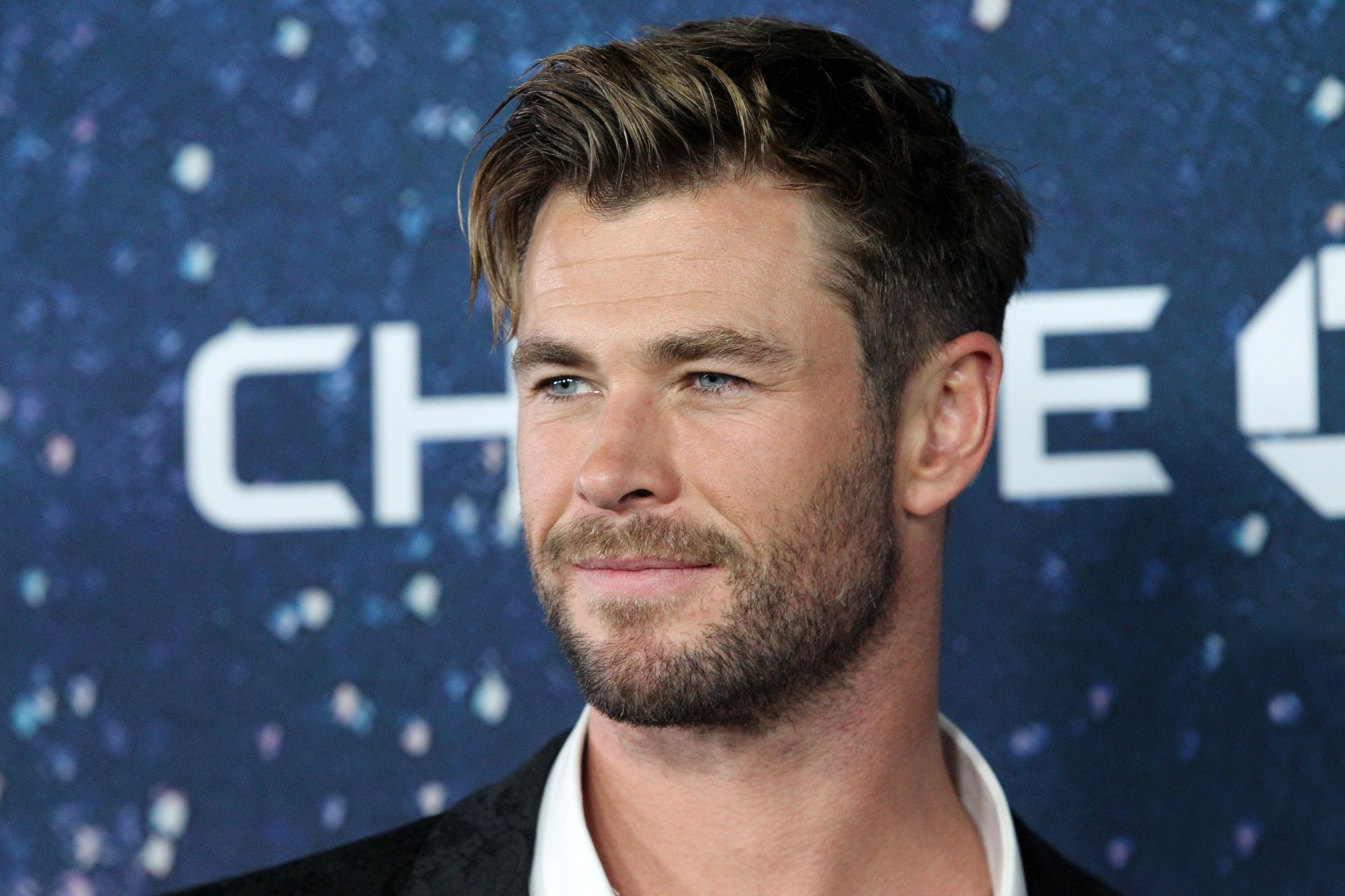 Chris Hemsworth, who stars in 'Thor: Love and Thunder,' wears a black suit over a white collared shirt.