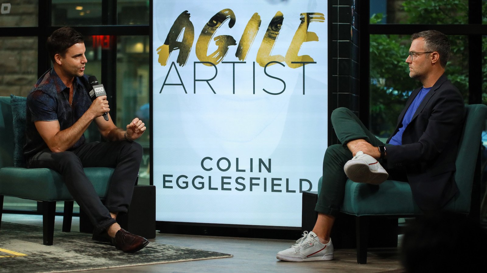 Colin Egglesfield sits with a microphone and talks about his book at Build Studio
