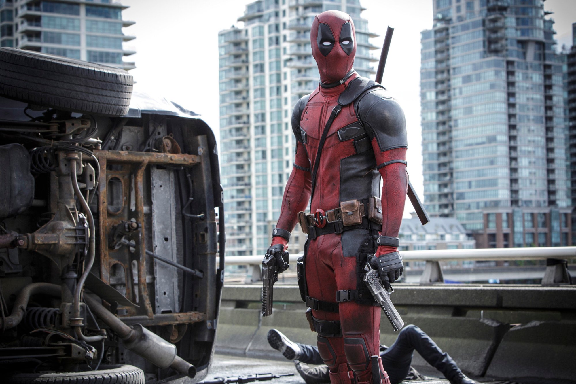 'Deadpool': Ryan Reynolds as Deadpool in costume, holding a gun in front of a flipped over car