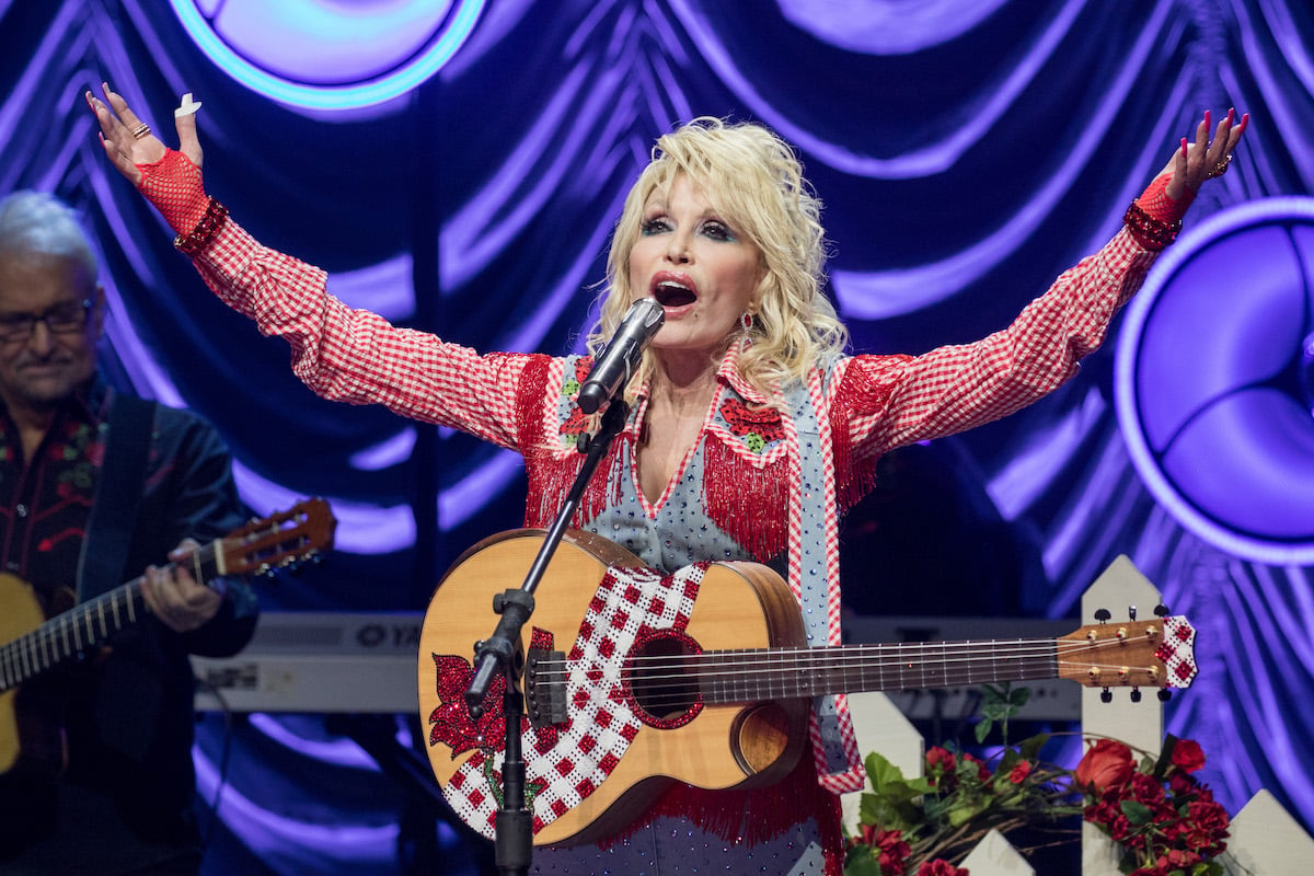 Dolly Parton performs on stage with a guitar.