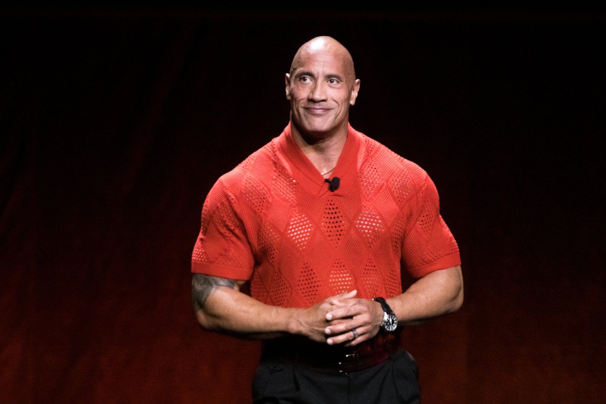 Dwayne Johnson, who has 3 kids, wearing a red shirt with his hands folded.