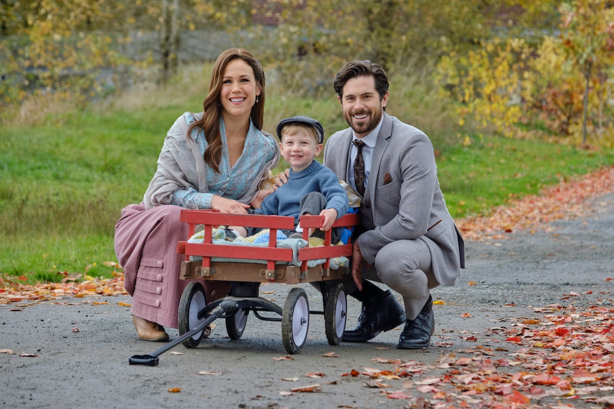 Elizabeth and Lucas crouching next to Little Jack in a red wagon in 'When Calls the Heart' Season 9 on Hallmark Channel