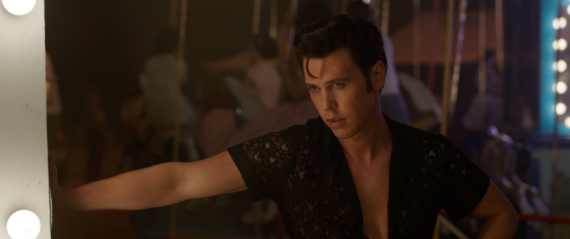 'Elvis' Austin Butler as Elvis Presley with the iconic hair, wearing black with production people rushing behind him