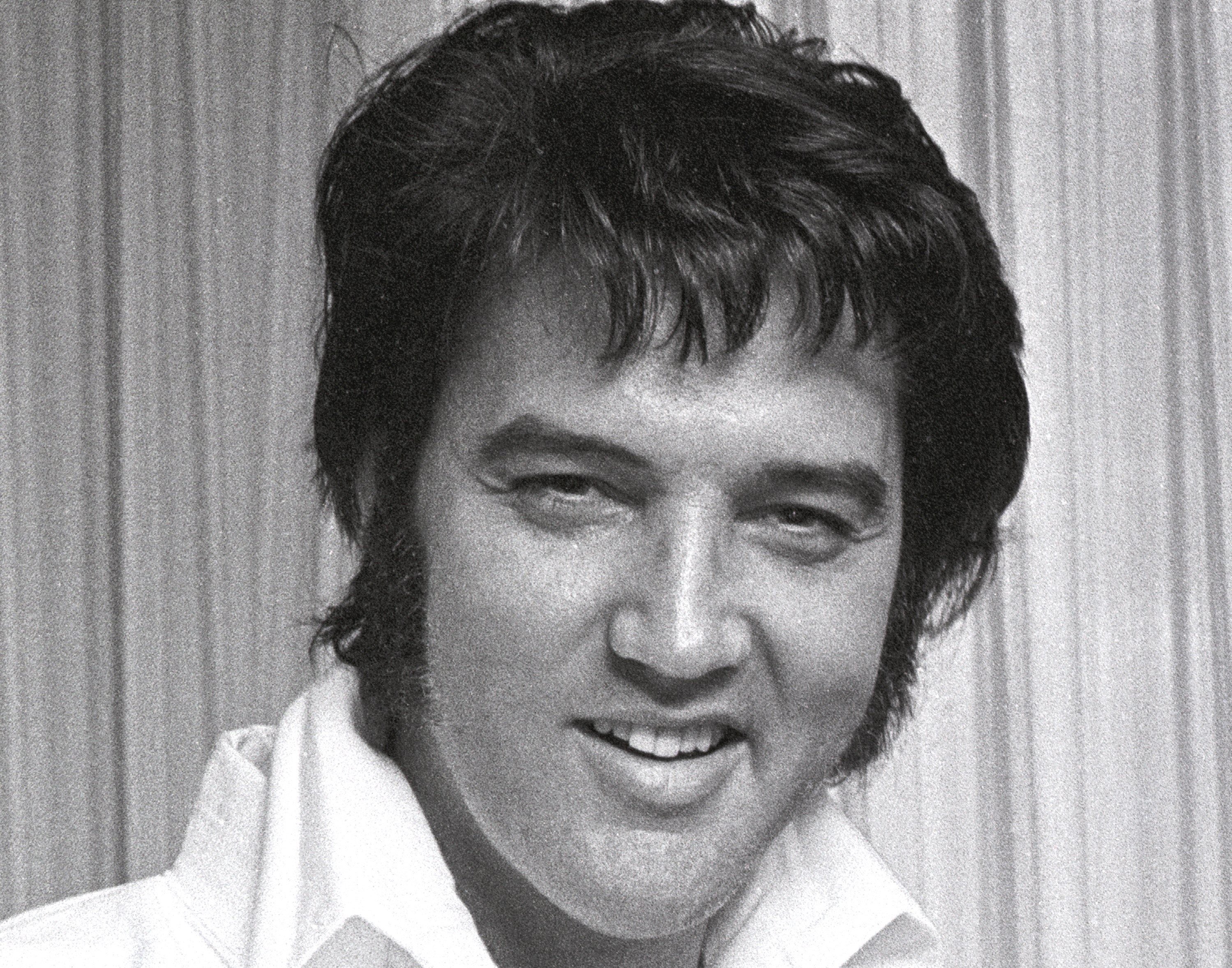 A black and white photo Elvis Presley smiling in the middle of a Karate workout in 1973.