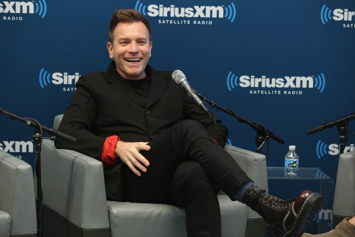 Ewan McGregor sitting down smiling while wearing a black suit.