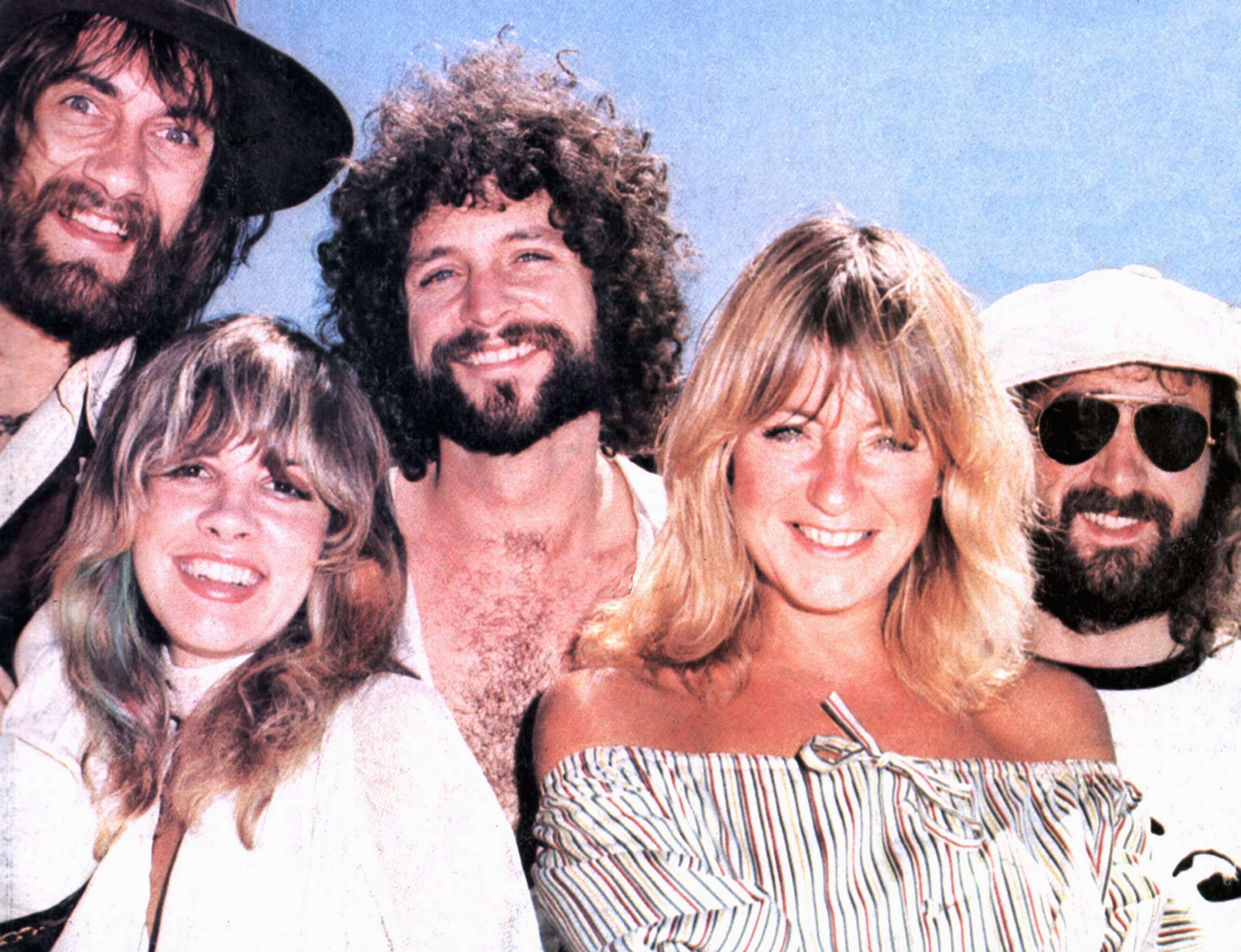 Mick Fleetwood, Stevie Nicks, Lindsey Buckingham, Christine McVie, and John McVie of Fleetwood Mac pose together against a blue background. 