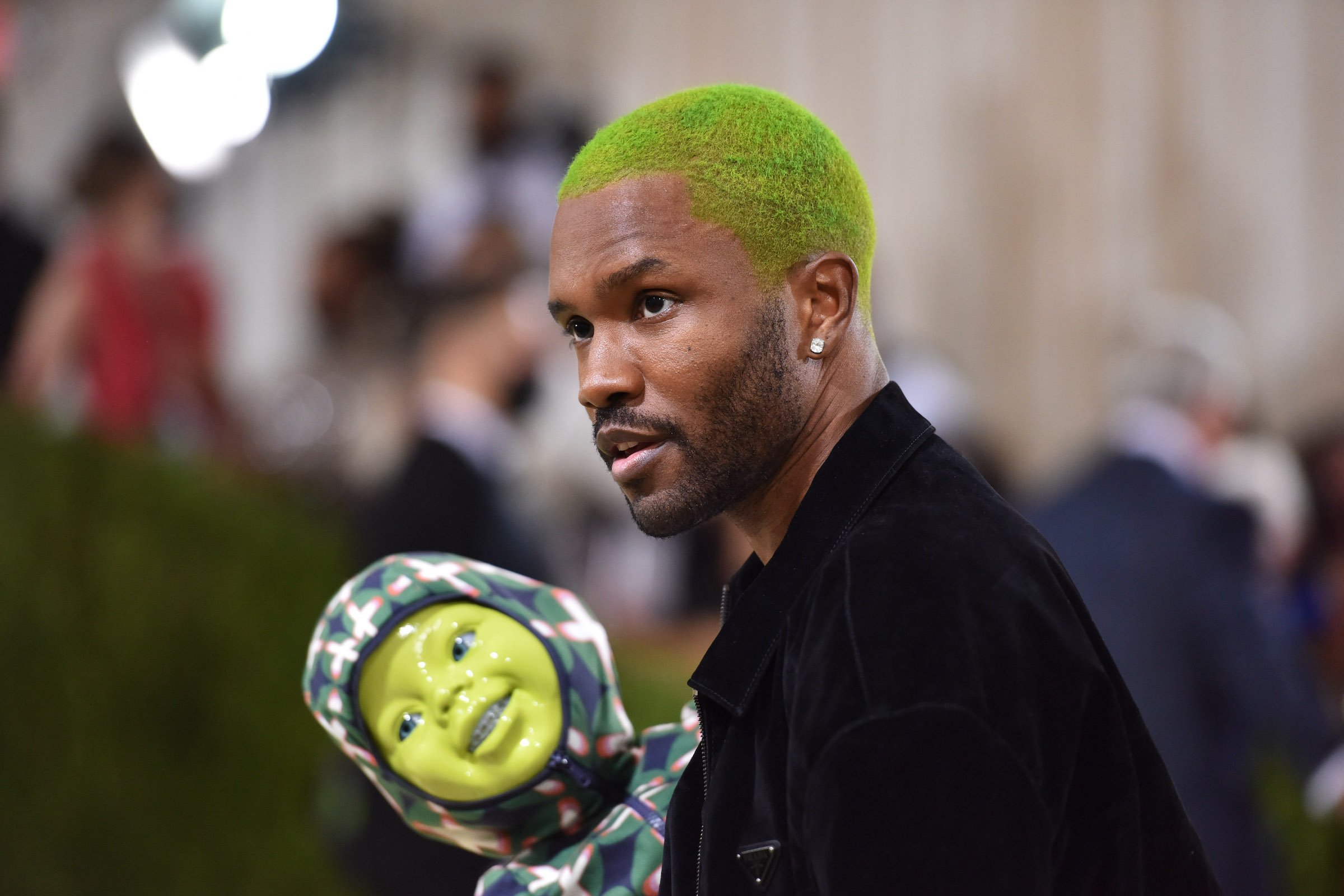 Frank Ocean, who is currently writing and directing a movie with A24, wearing a black suit and holding a green baby doll
