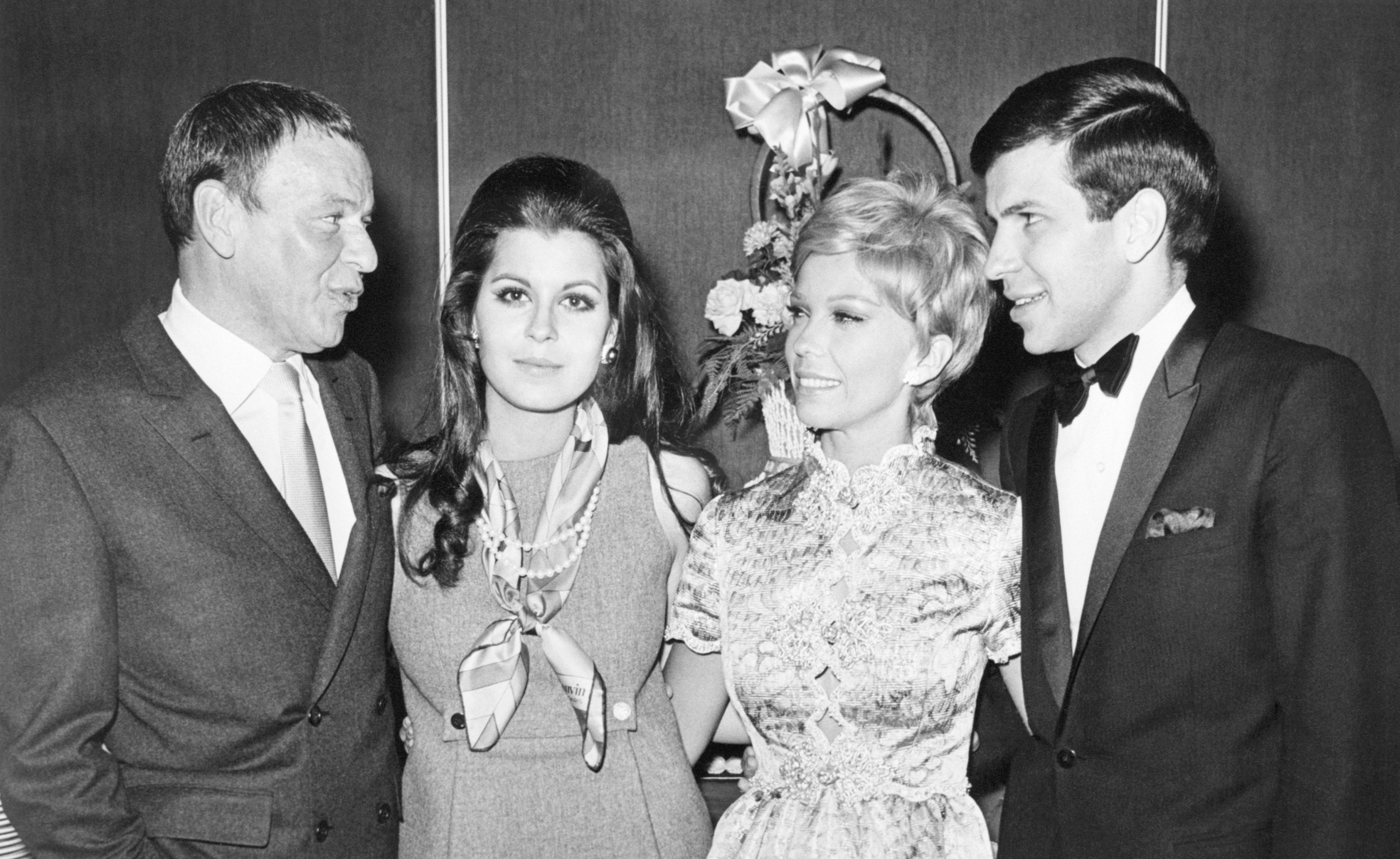 A black and white photo of Frank Sinatra and his daughters Tina and Nancy, and his son Frank, standing with their arms together.