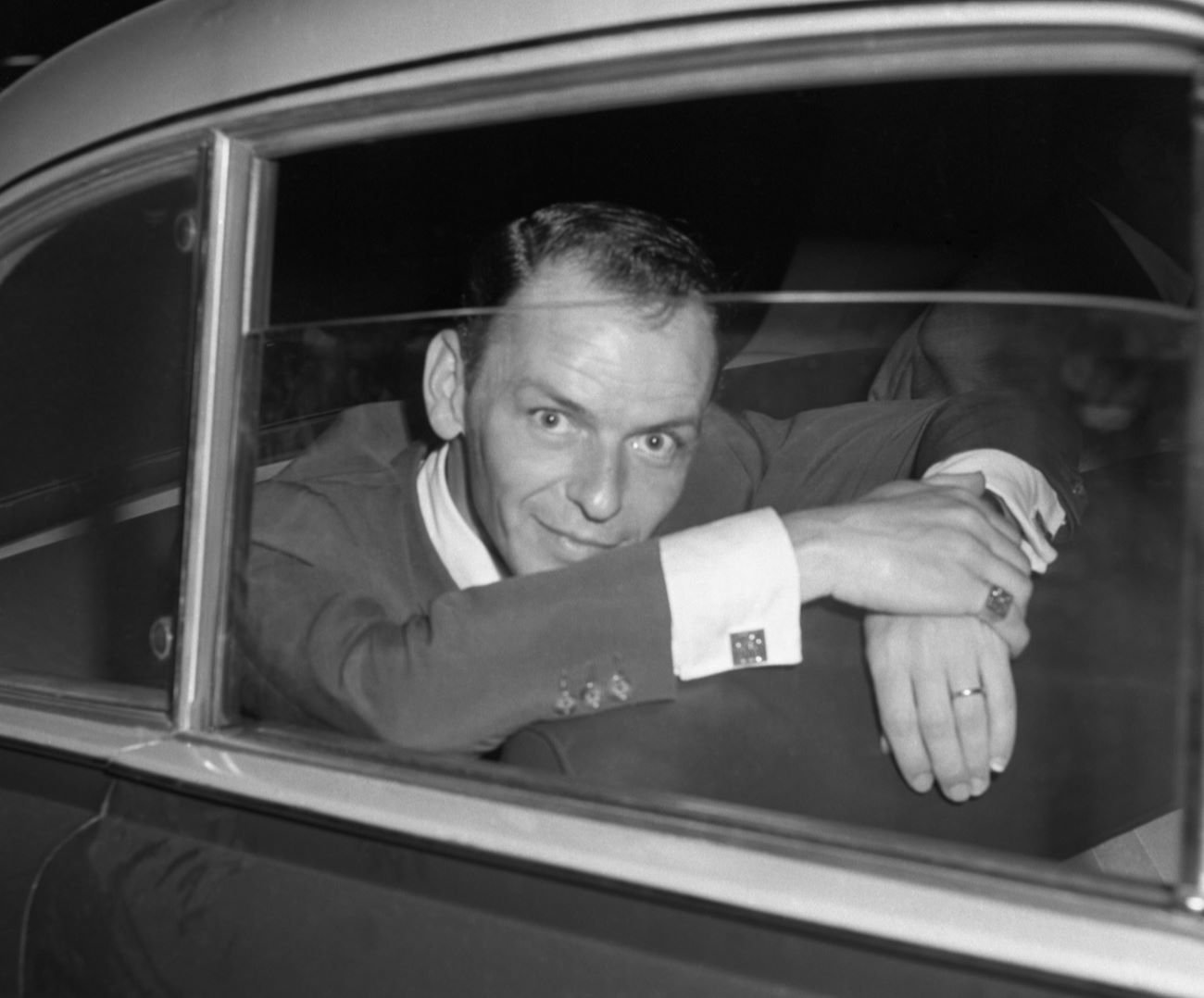 A black and white picture of Frank Sinatra sitting in the back seat of a car.