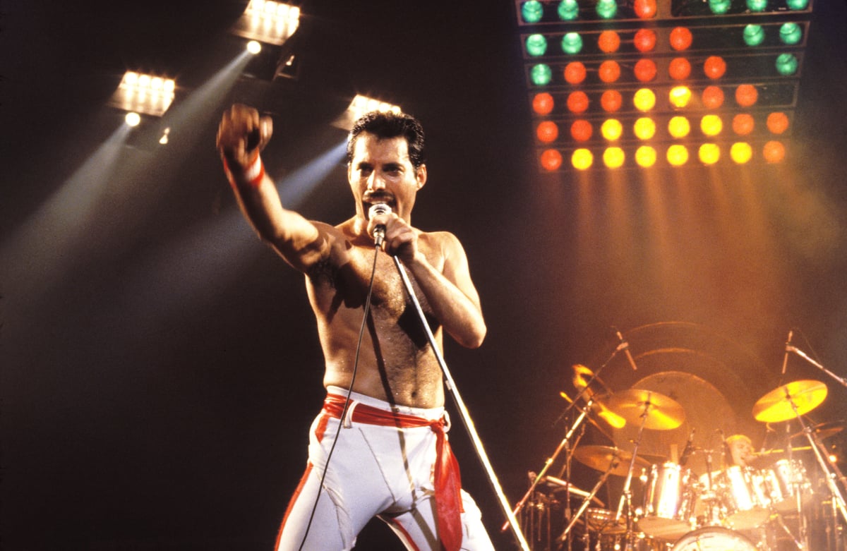 Freddie Mercury of Queen makes a fist on stage as he sings into a microphone.