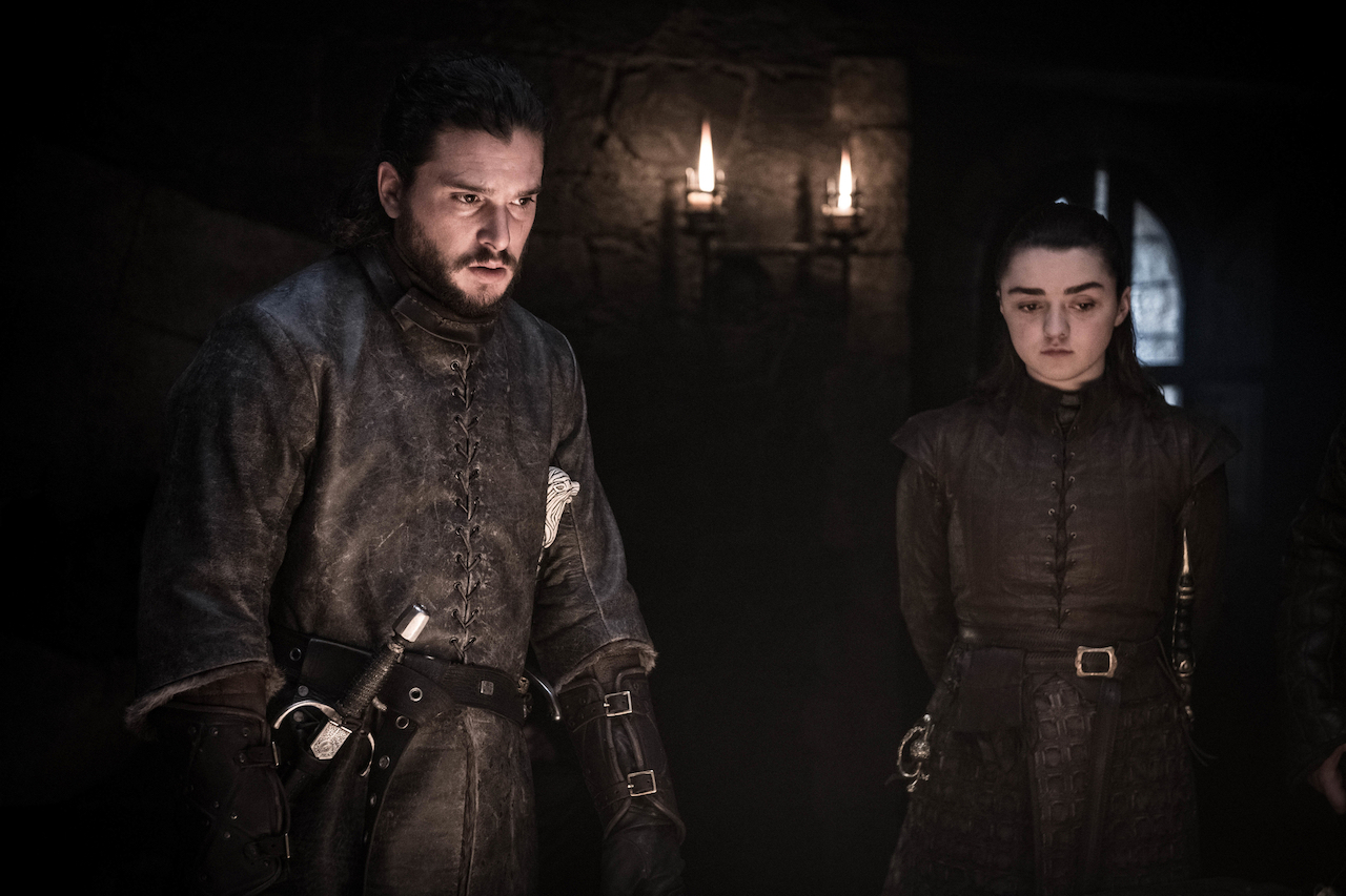 Kit Harington as Jon Snow and Maisie Williams as Arya Stark stand in a dark room talking in 'Game of Thrones'.