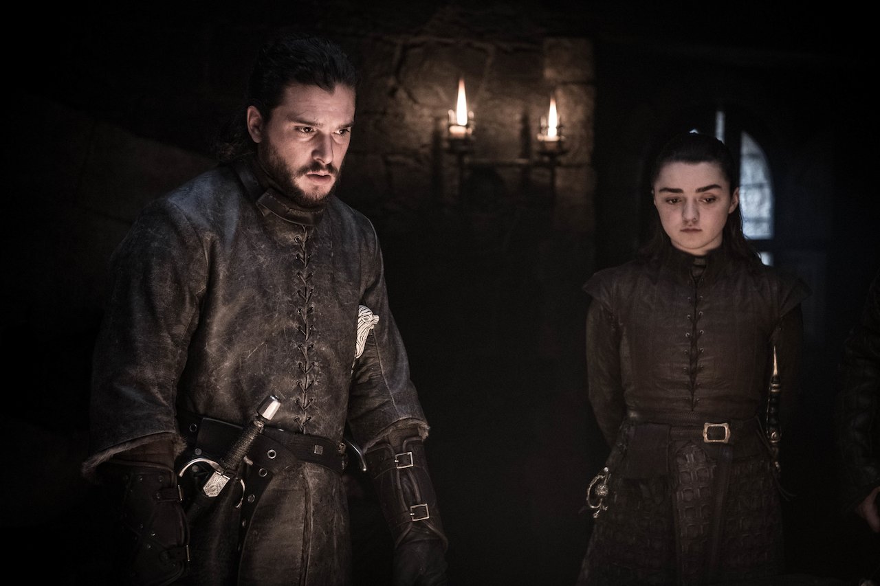 Kit Harington as Jon Snow and Maisie Williams as Arya Stark stand in a dark room talking in 'Game of Thrones'.