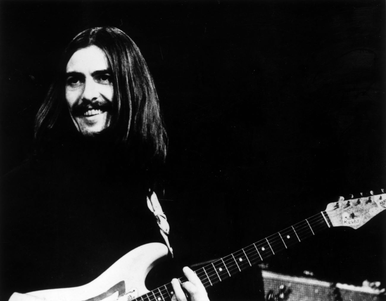 A black and white picture of George Harrison with a guitar.