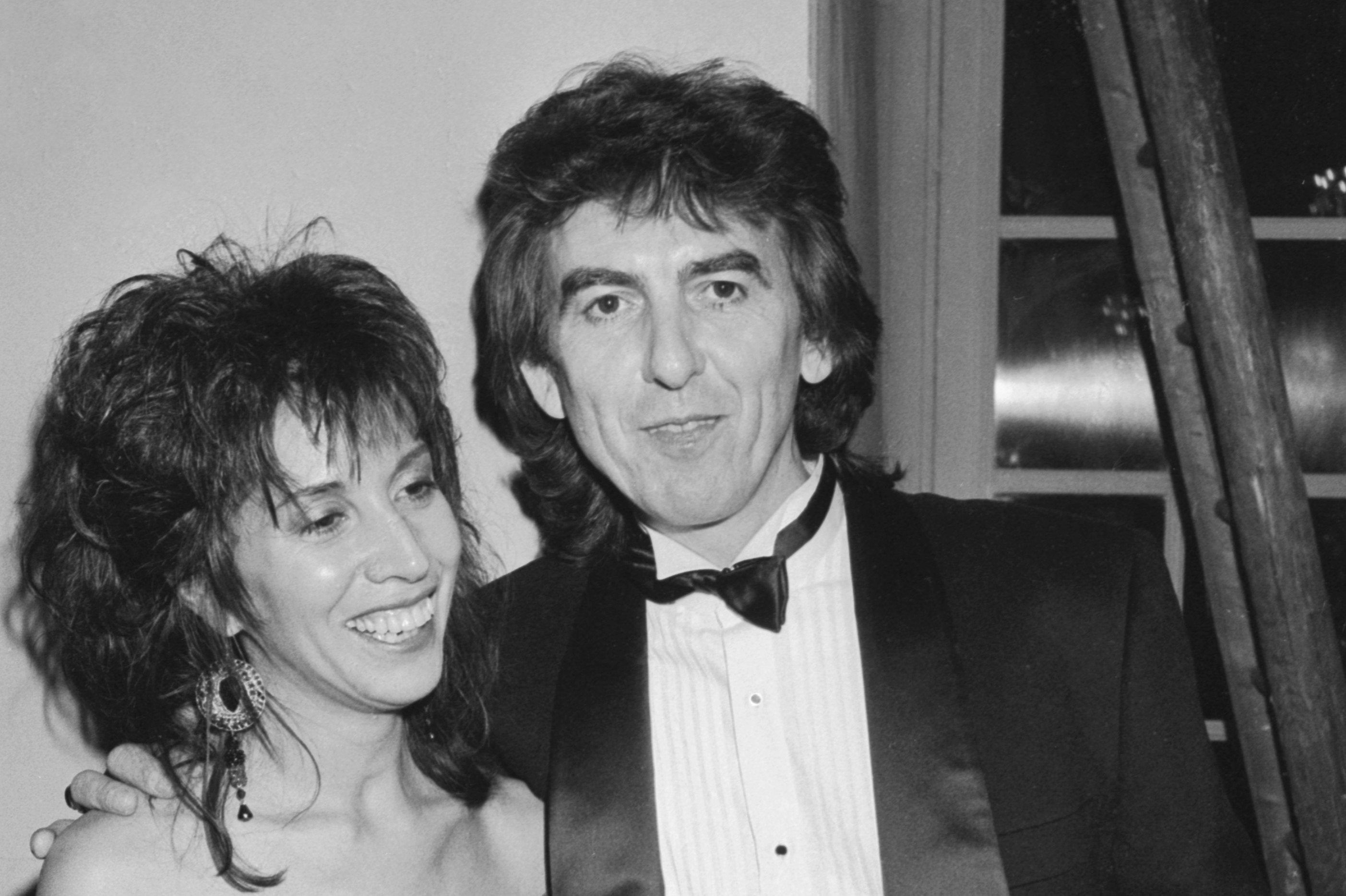 A black and white picture of George Harrison in a tuxedo with his arm around his wife Olivia Harrison's shoulders.