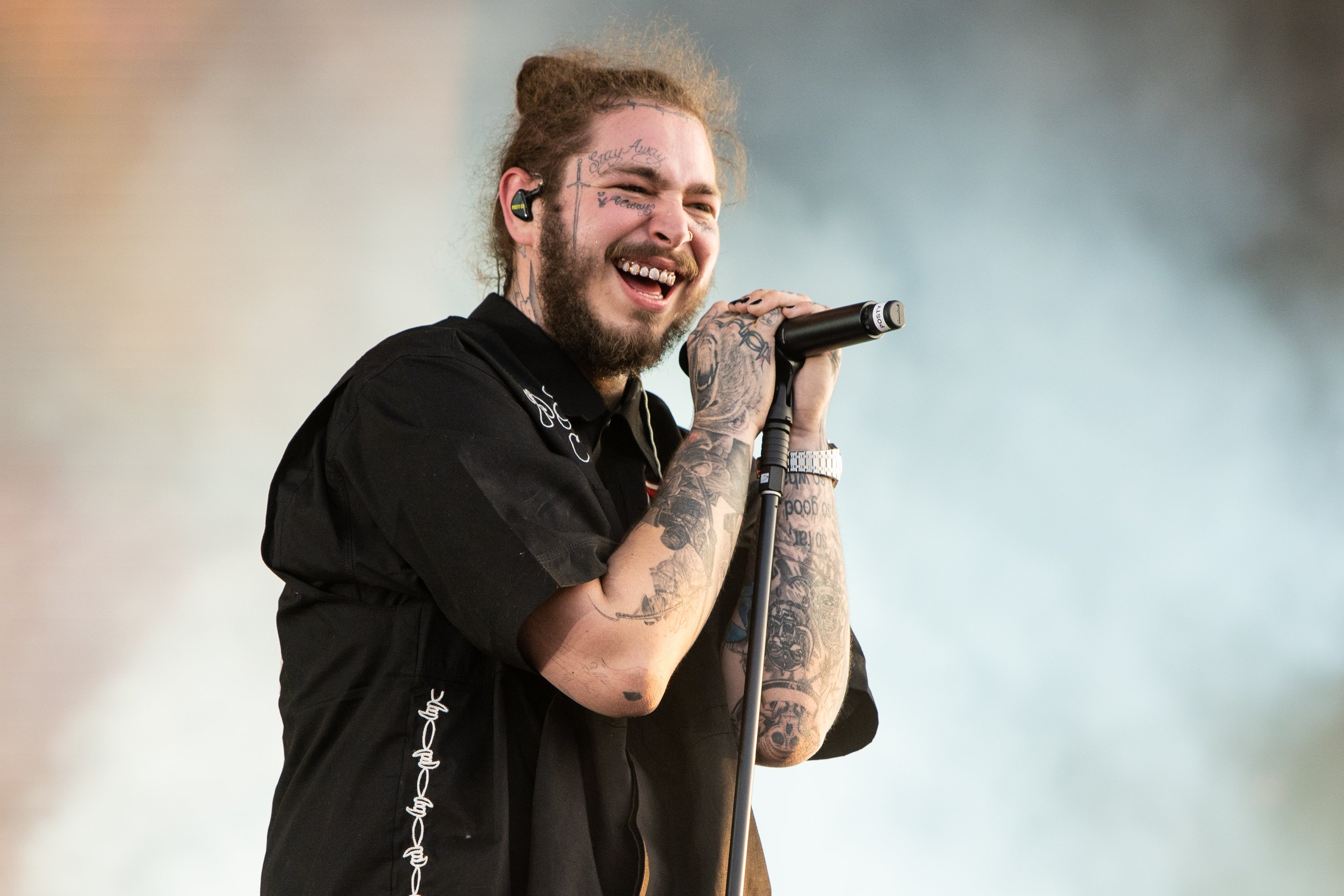 Post Malone, who recently exchanged tattoos with The Kid Laroi, performing wearing a black shirt against a white background