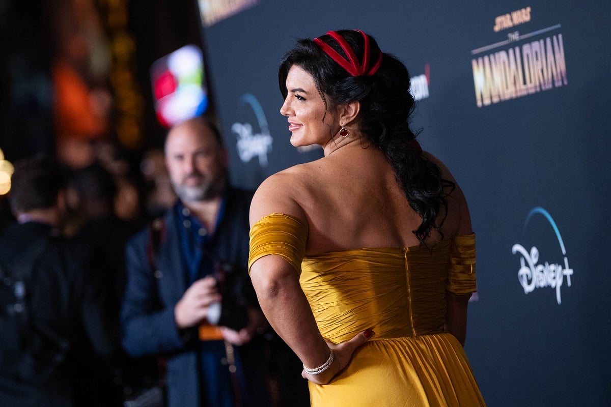 Gina Carano smiling while wearing a yellow dress.