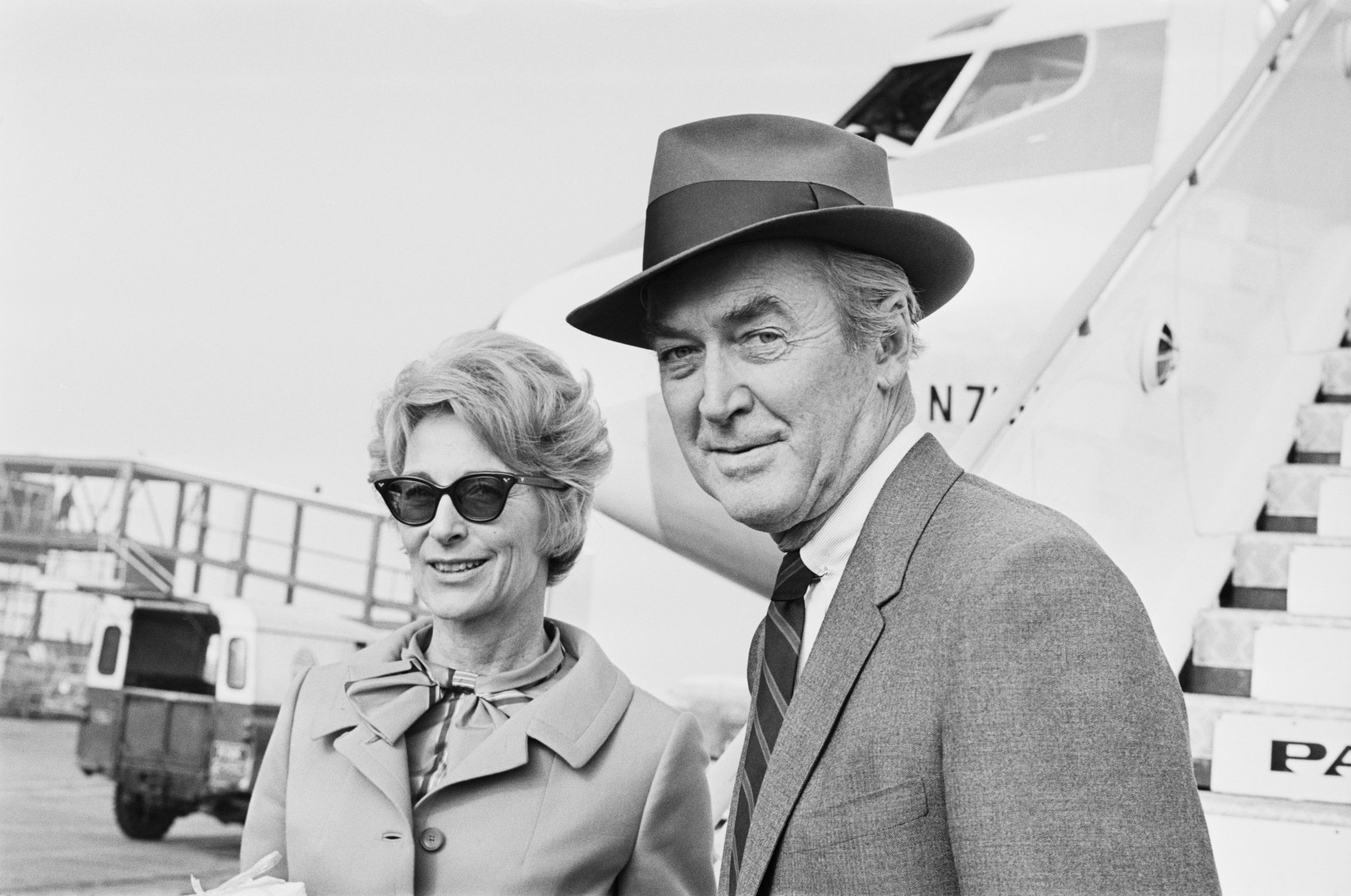 Gloria Hatrick McLean and Jimmy Stewart smiling in front of an airplane
