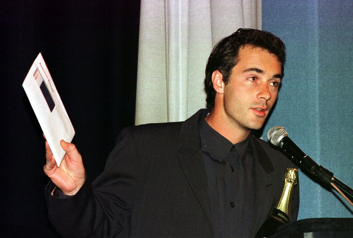 Greg Wise speaking on stage while wearing a suit.