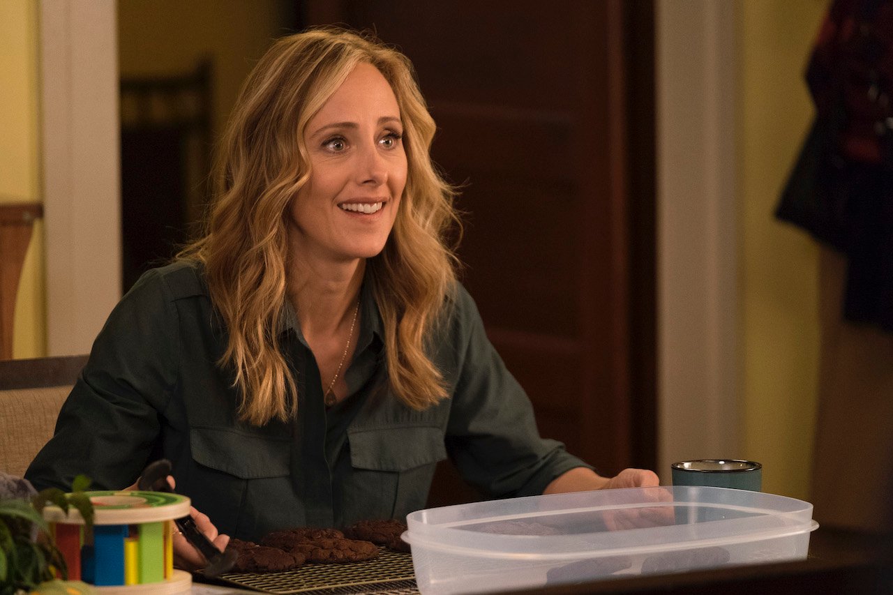 Kim Raver as Teddy Altman sits at a table smiling in 'Grey's Anatomy'.