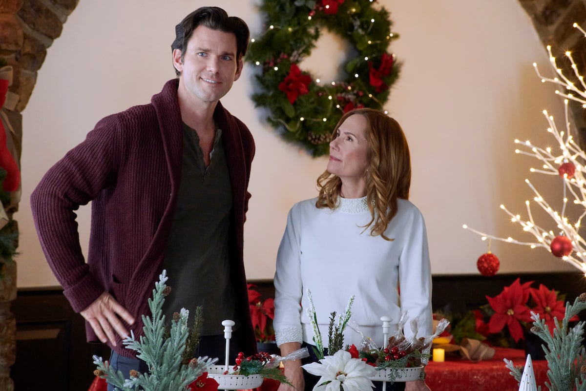 Kevin McGarry and Kayla Wallace standing in front of a holiday wreath in the 2022 Hallmark Christmas in July movie 'My Grown-Up Christmas List'