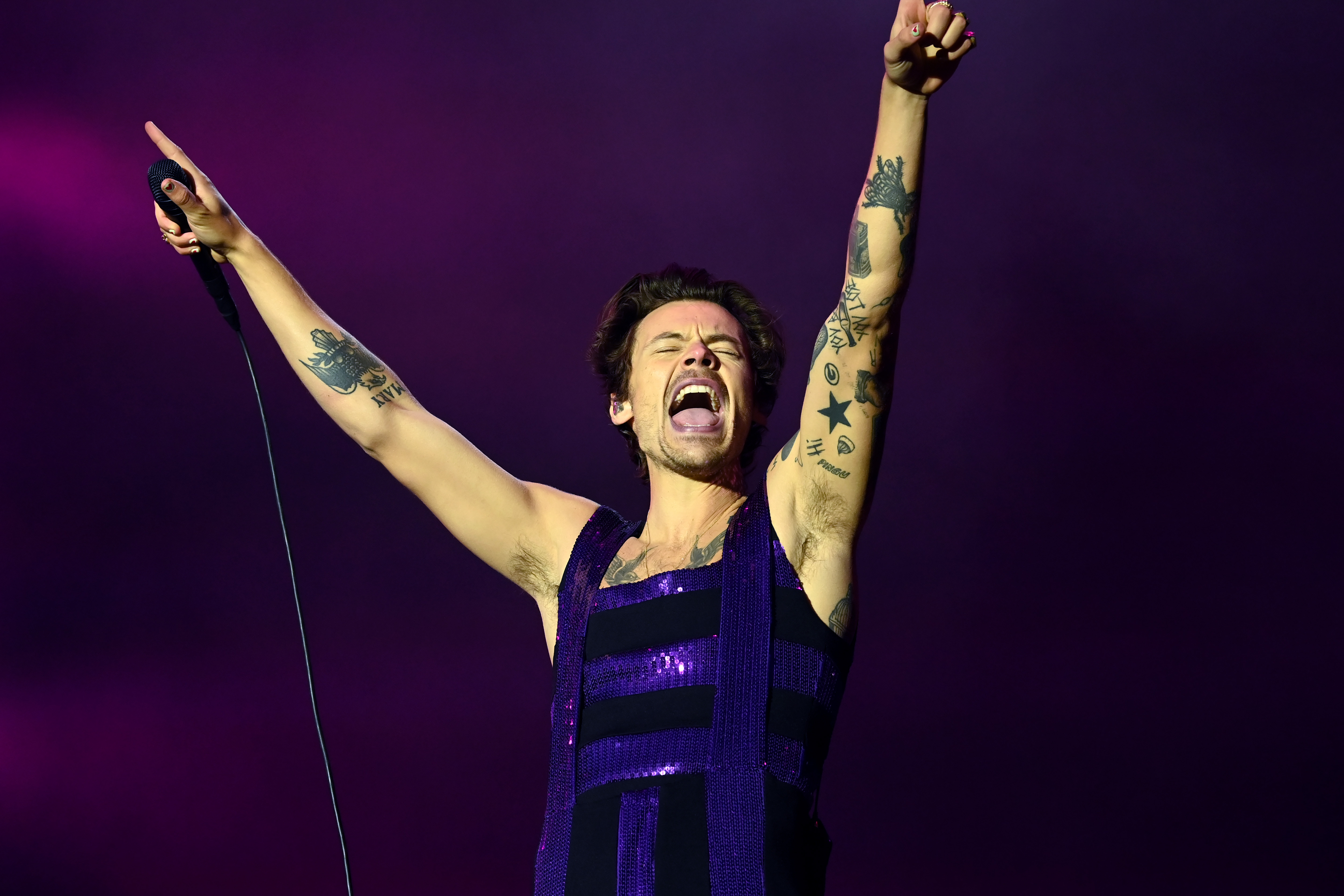 'Harry's House' artist Harry Styles performing, with his arms raised and holding a microphone