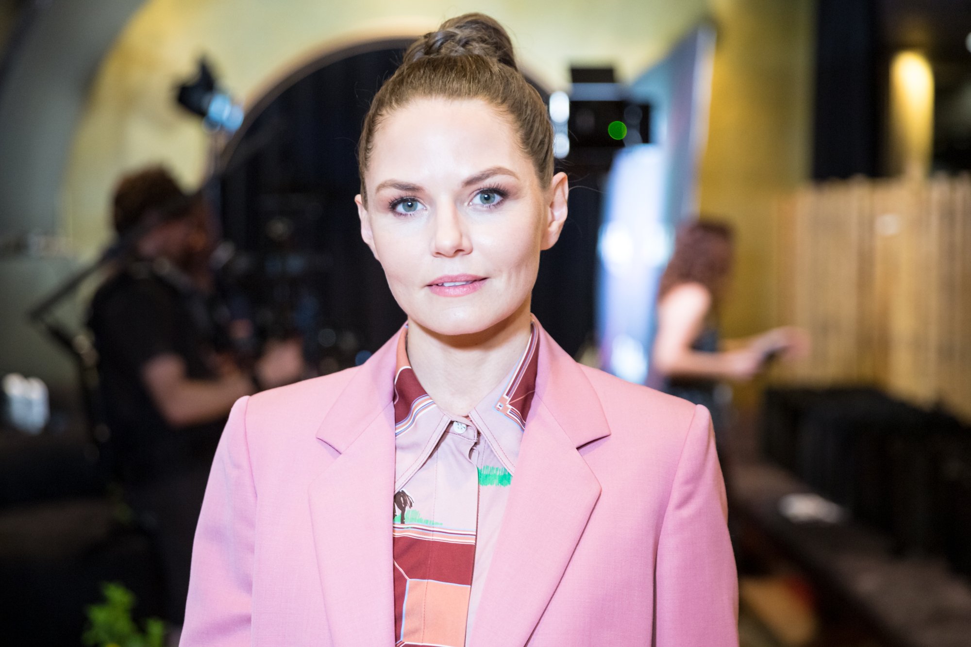 'This Is Us' star Jennifer Morrison. She's wearing a blouse with different shades of pink and a pink blazer. Her hair is pulled into a bun, and she's looking directly at the camera.