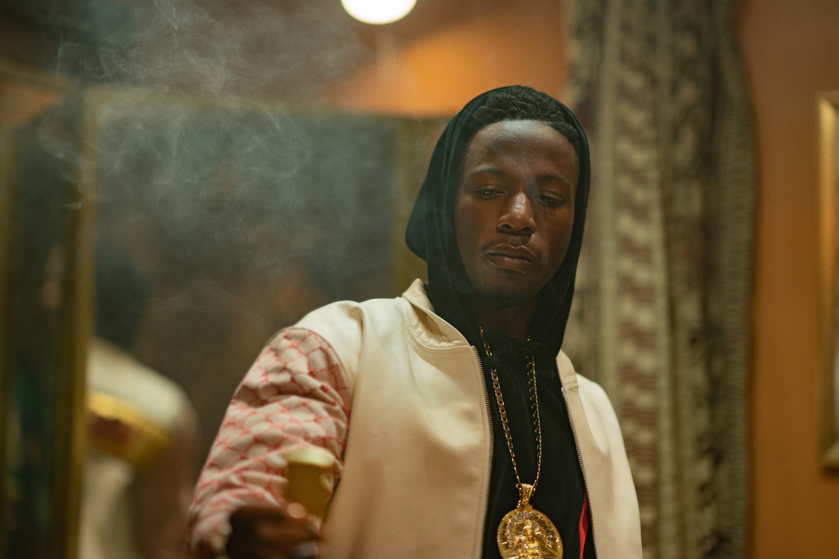 Joey Bada$$ as Unique smoking and looking at an object in 'Power Book III: Raising Kanan'