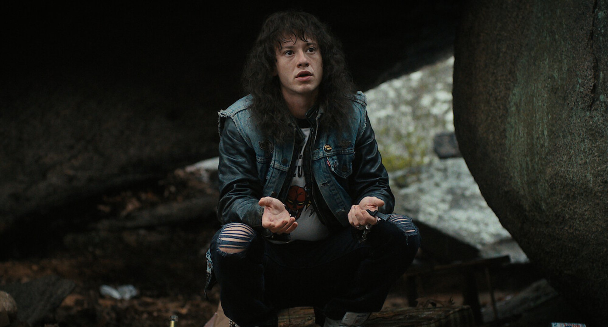 Joseph Quinn as a teenage Eddie Munson in 'Stranger Things' Season 4 sitting in the woods.