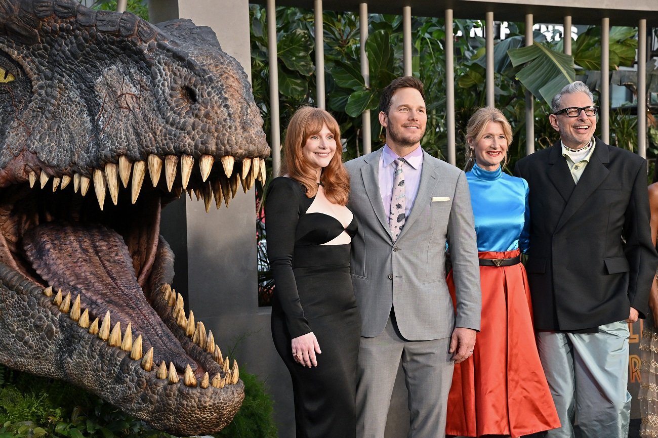 'Jurassic World: Dominion' cast members Bryce Dallas Howard, Chris Pratt, Laua Dern, and Jeff Goldblum pose next to a dinosaur statue.