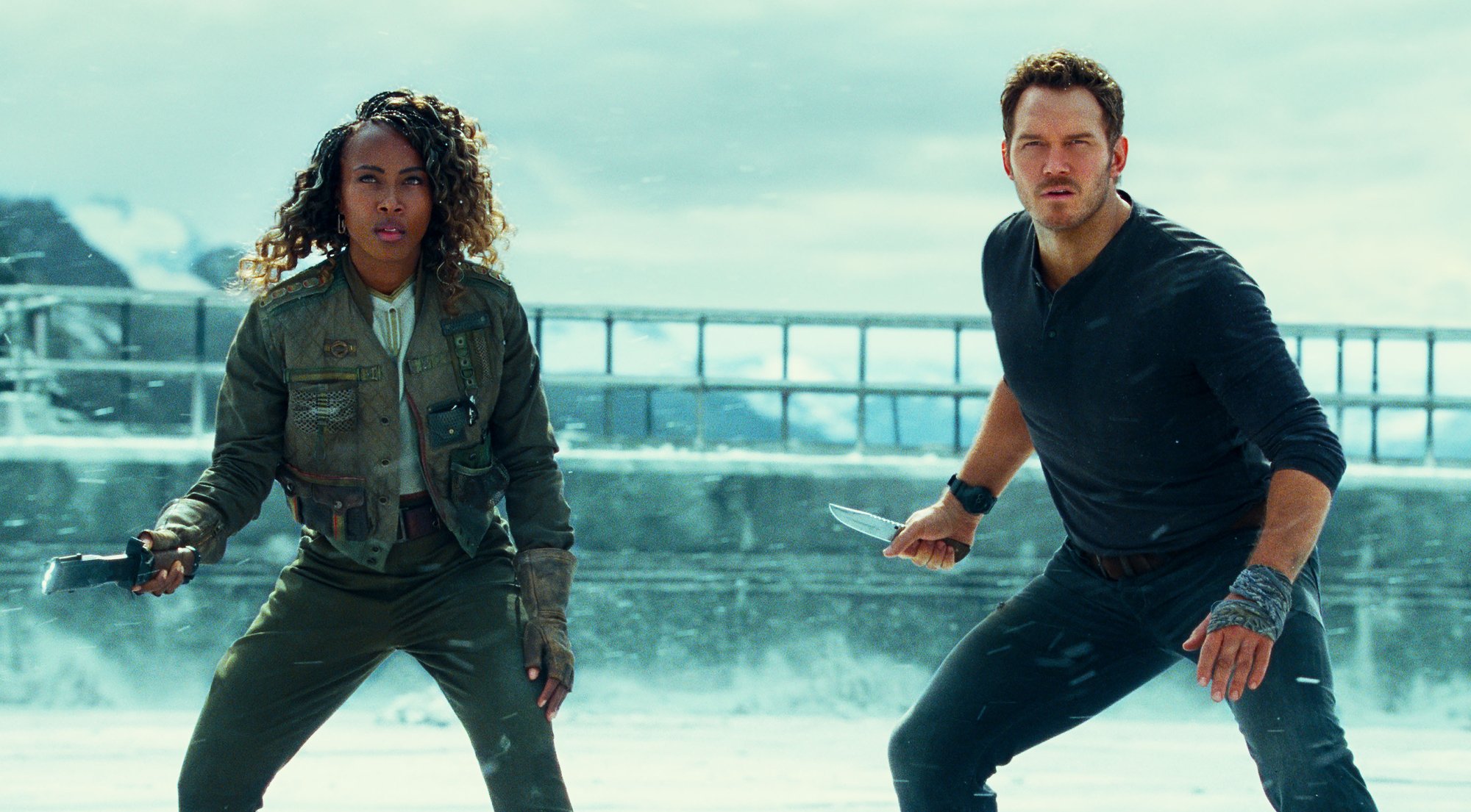 'Jurassic World Dominion' stars DeWanda Wise as Kayla Watts holding an electric stick and Chris Pratt as Owen Grady holding a knife, ready to fight in snow landscape