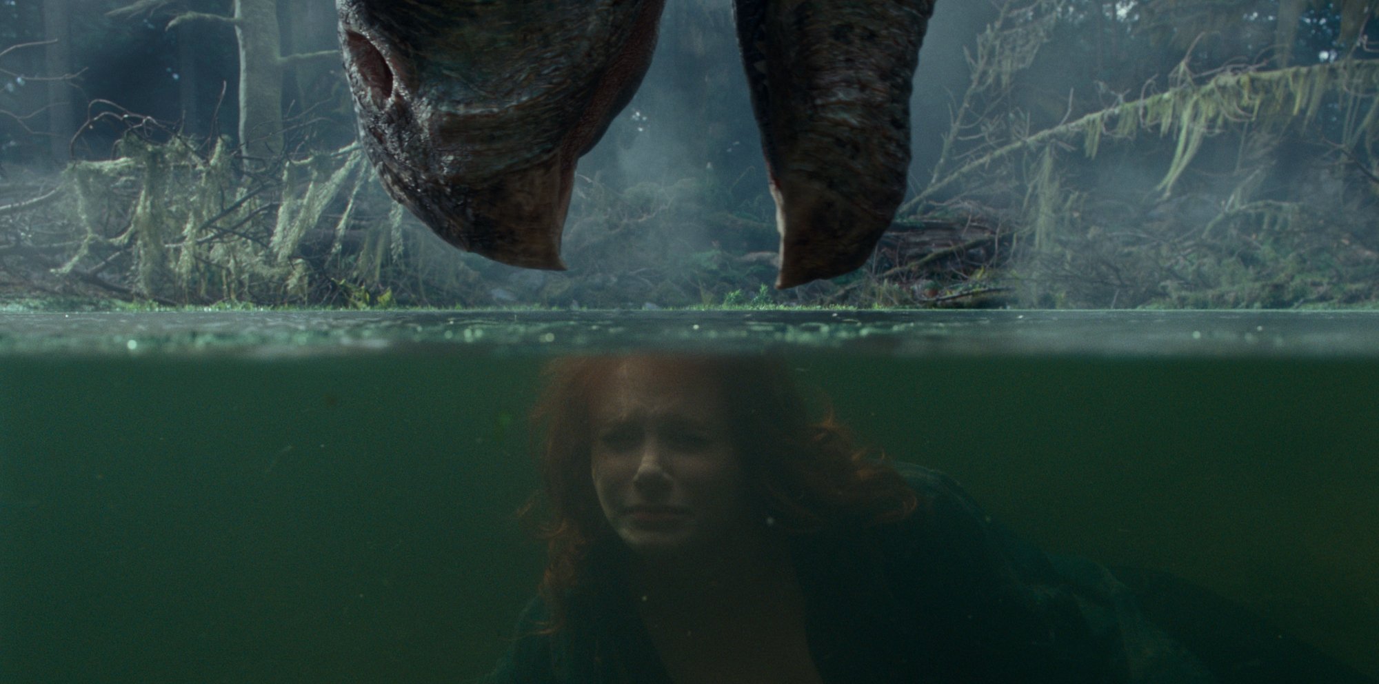 'Jurassic World Dominion' Therizinosaurus and Bryce Dallas Howard as Claire Dearing. The Therizinosaurus is lowering its mouth toward the water with Howard holding her breath under water.