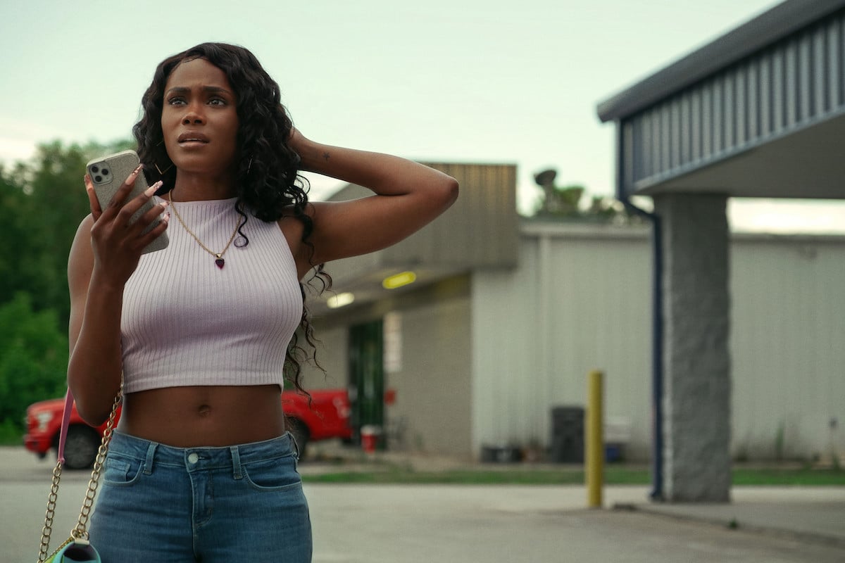 Shannon Thornton appears as her character Keyshawn in 'P-Valley.' She's standing outside of a dollar store wearing a crop top and jeans with her phone in her hand.