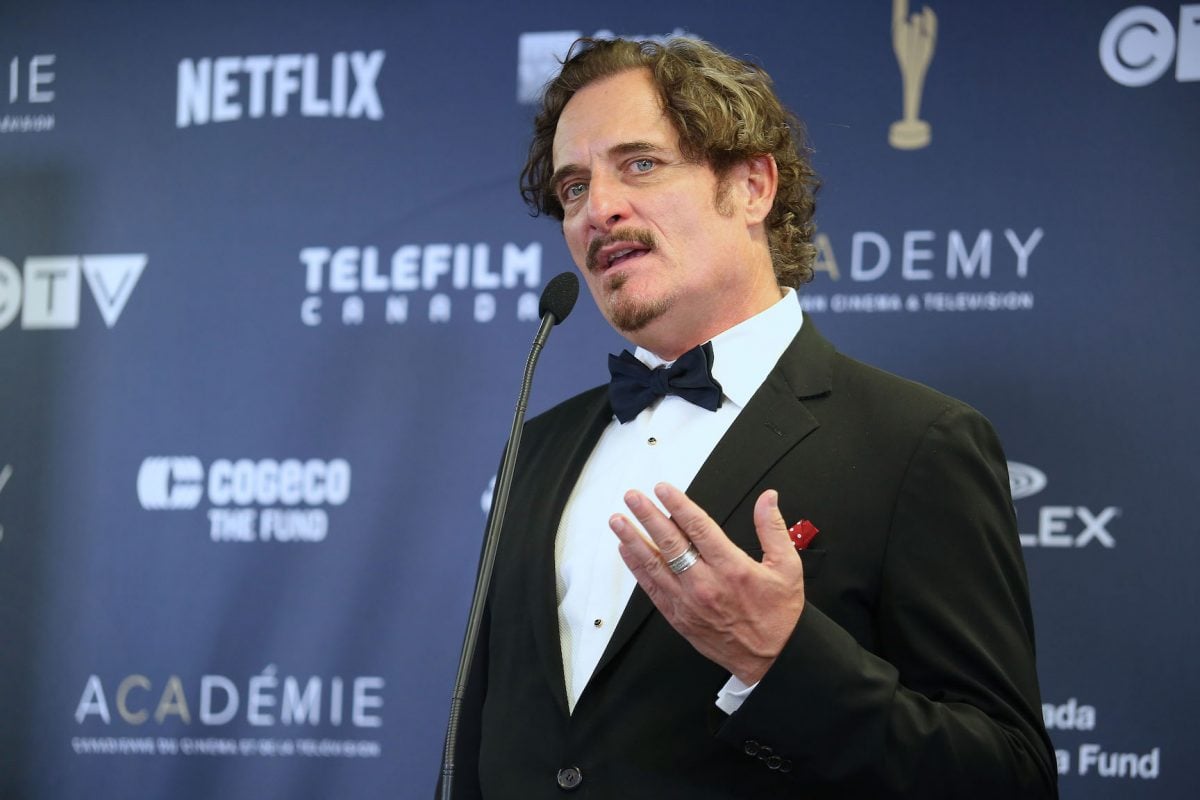 Kim Coates speaking into a microphone while dressed in a tuxedo at an event
