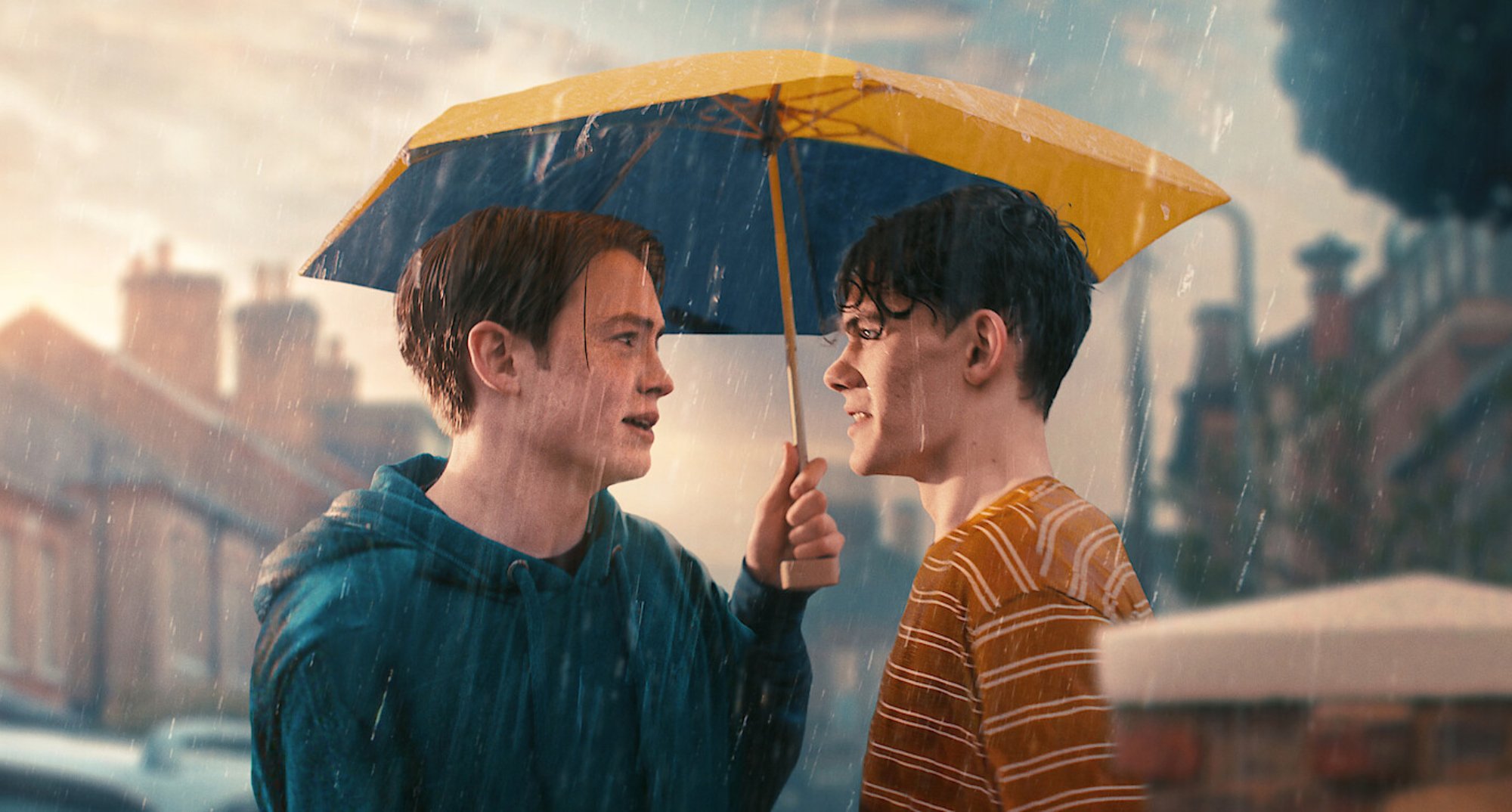 Kit Connor and Joe Locke in 'Heartstopper' in the rain with an umbrella.
