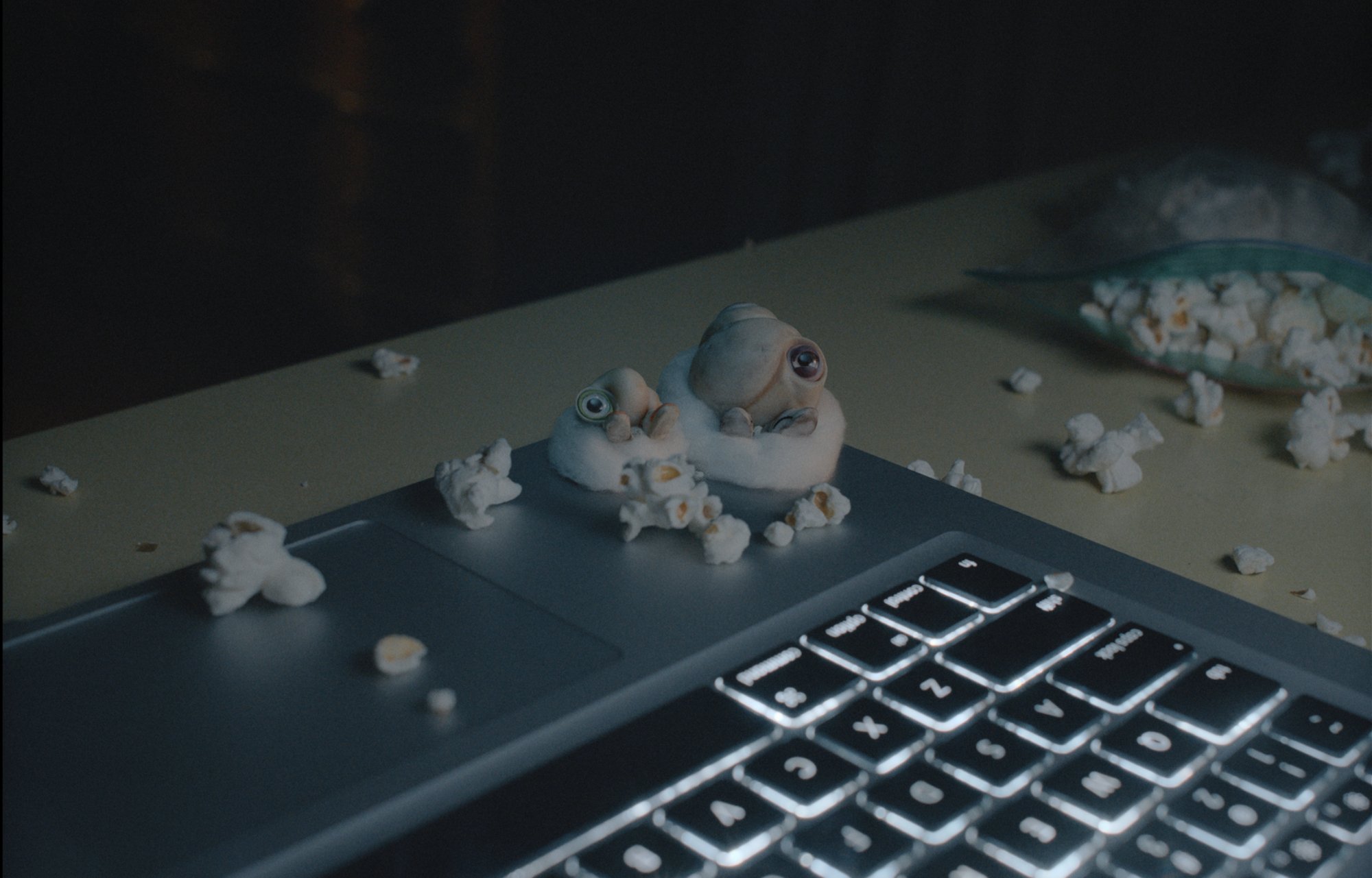 'Marcel the Shell With Shoes On' Marcel (voiced by Jenny Slate) and Connie (voiced by Isabella Rossellini) sitting on balls of cotton on a laptop, watching the screen, while surrounded by popcorn.