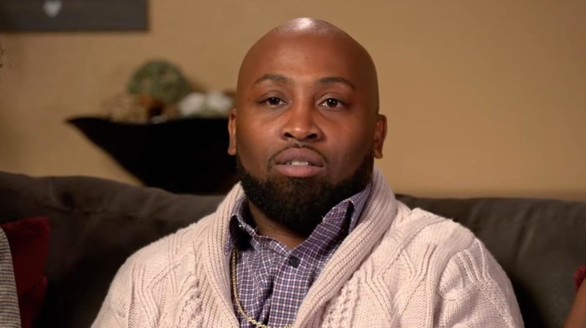 Marcus Epps wearing a white cardigan while sitting on a couch for 'Seeking Sister Wife' Season 4 interviews on TLC.