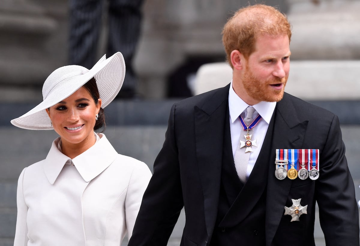 Meghan Markle and Prince Harry, who would've, according to an author, been cleared to take a break by Queen Elizabeth II, smile and look on