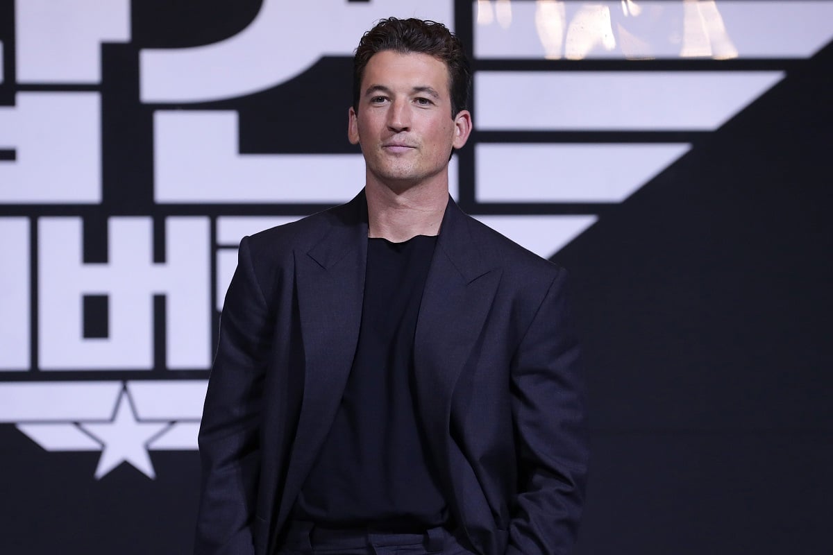 Miles Teller smirking while wearing a black suit.