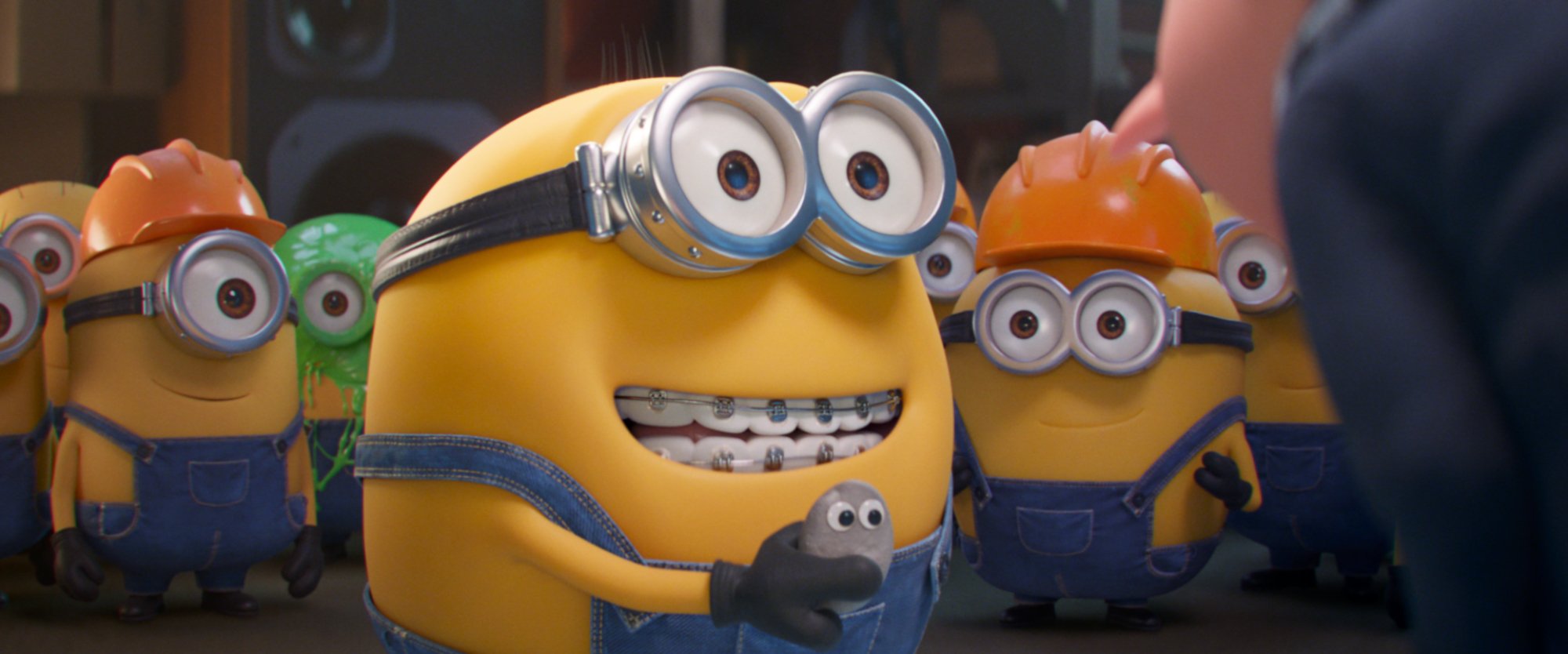 'Minions: The Rise of Guru' Minion Otto smiling while wearing braces and holding a rock with googly eyes